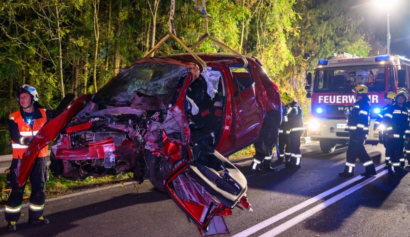 Schwer beschädigtes Auto wird nach Unfall von Feuerwehr geborgen, Einsatzkräfte stehen daneben.