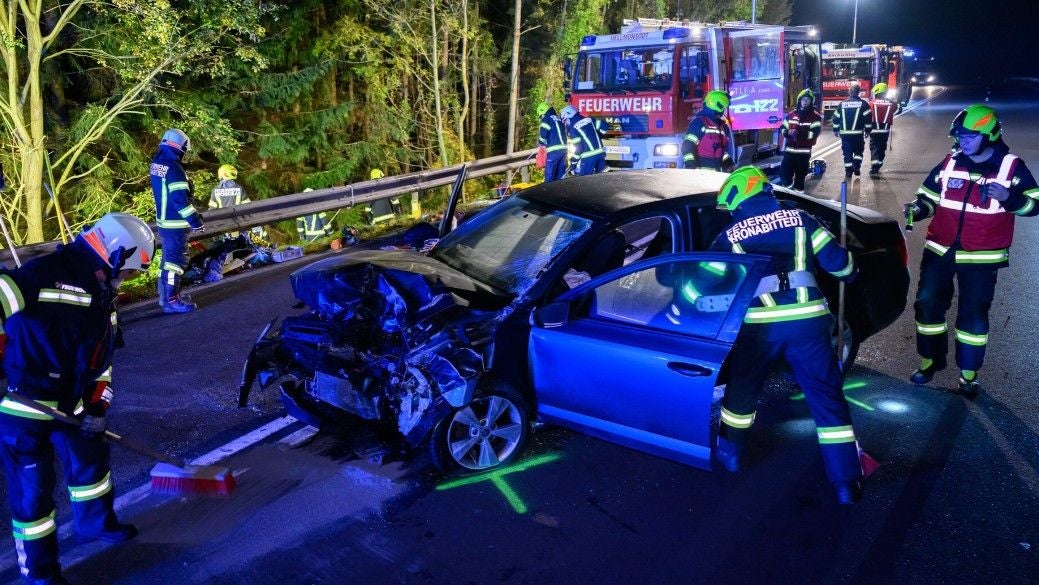 Feuerwehrleute räumen nach Verkehrsunfall ein zerstörtes Auto auf einer nächtlichen Straße.