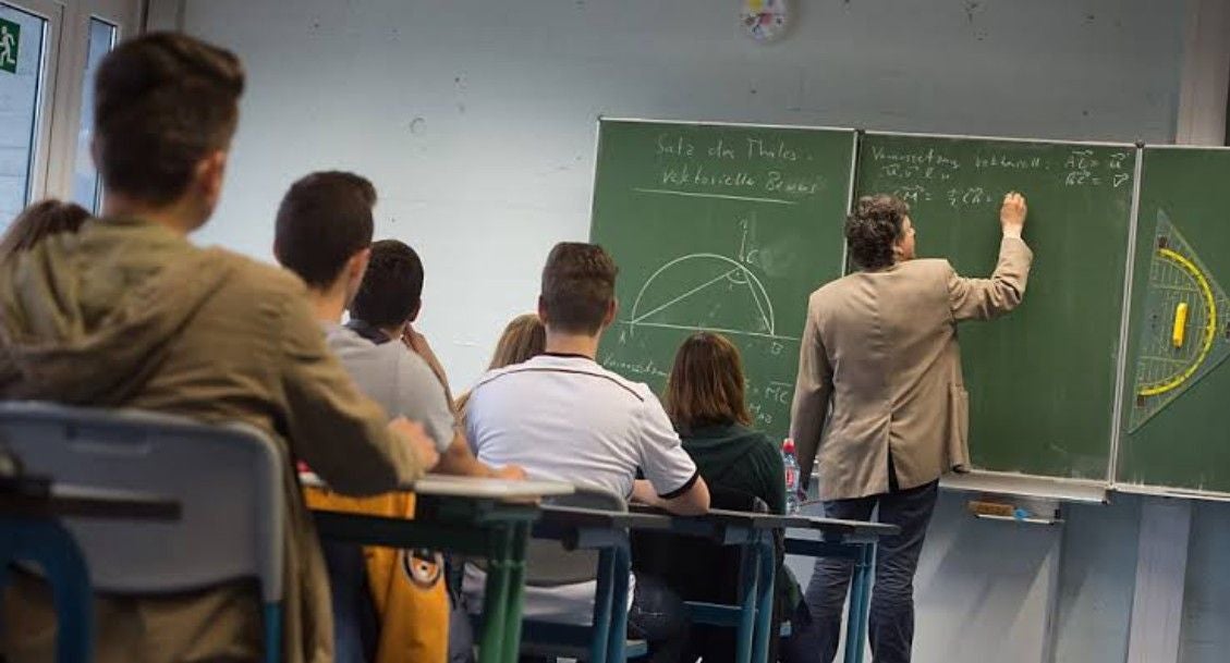 Lehrer schreibt Mathematik an die Tafel, Schüler sitzen im Klassenzimmer und schauen zu.