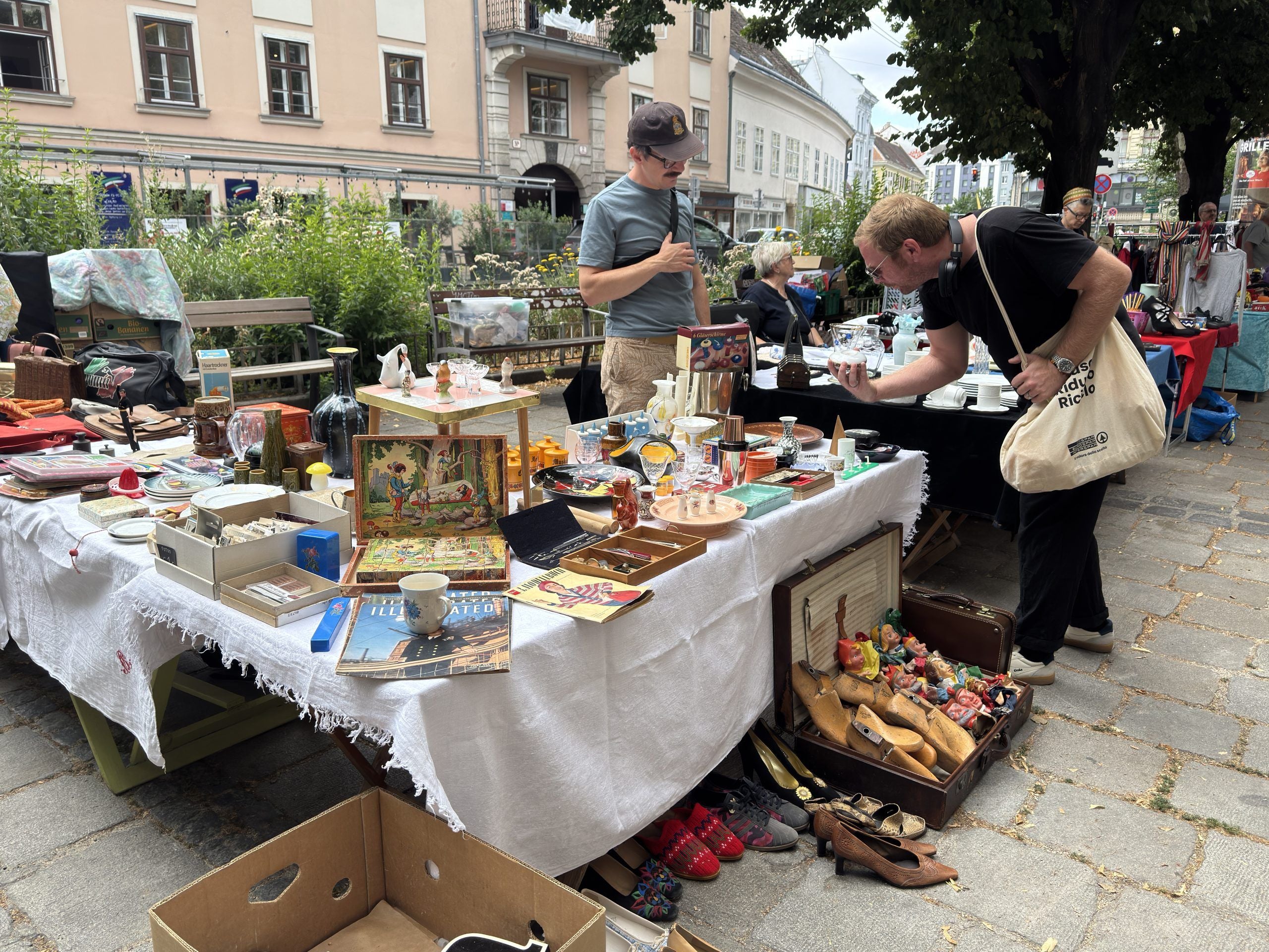 Zwei Männer stöbern auf einem Flohmarkt an einem Tisch mit verschiedenen Secondhand-Artikeln.