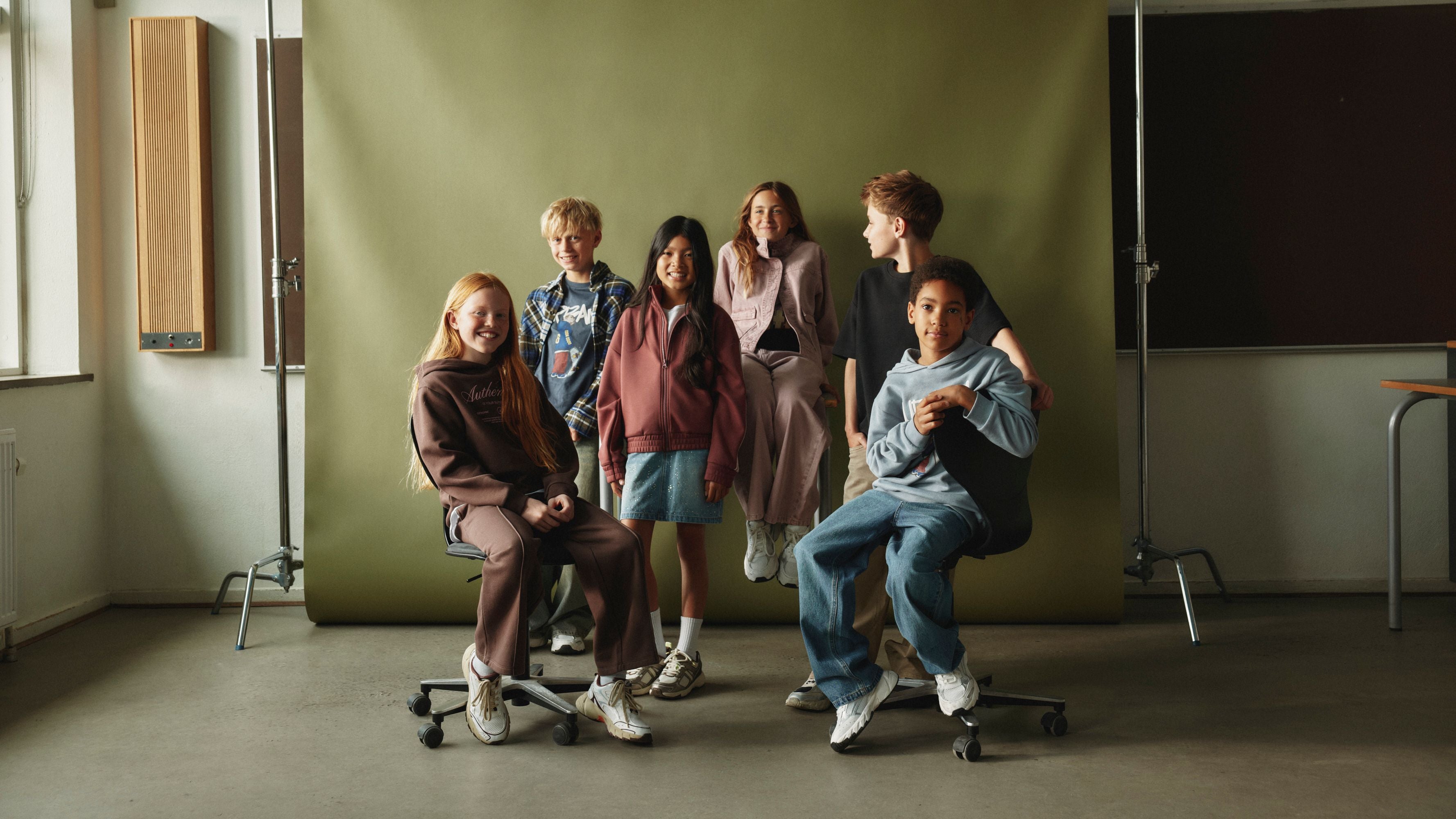 Sechs Kinder posieren lachend vor einem grünen Hintergrund in einem Klassenraum.