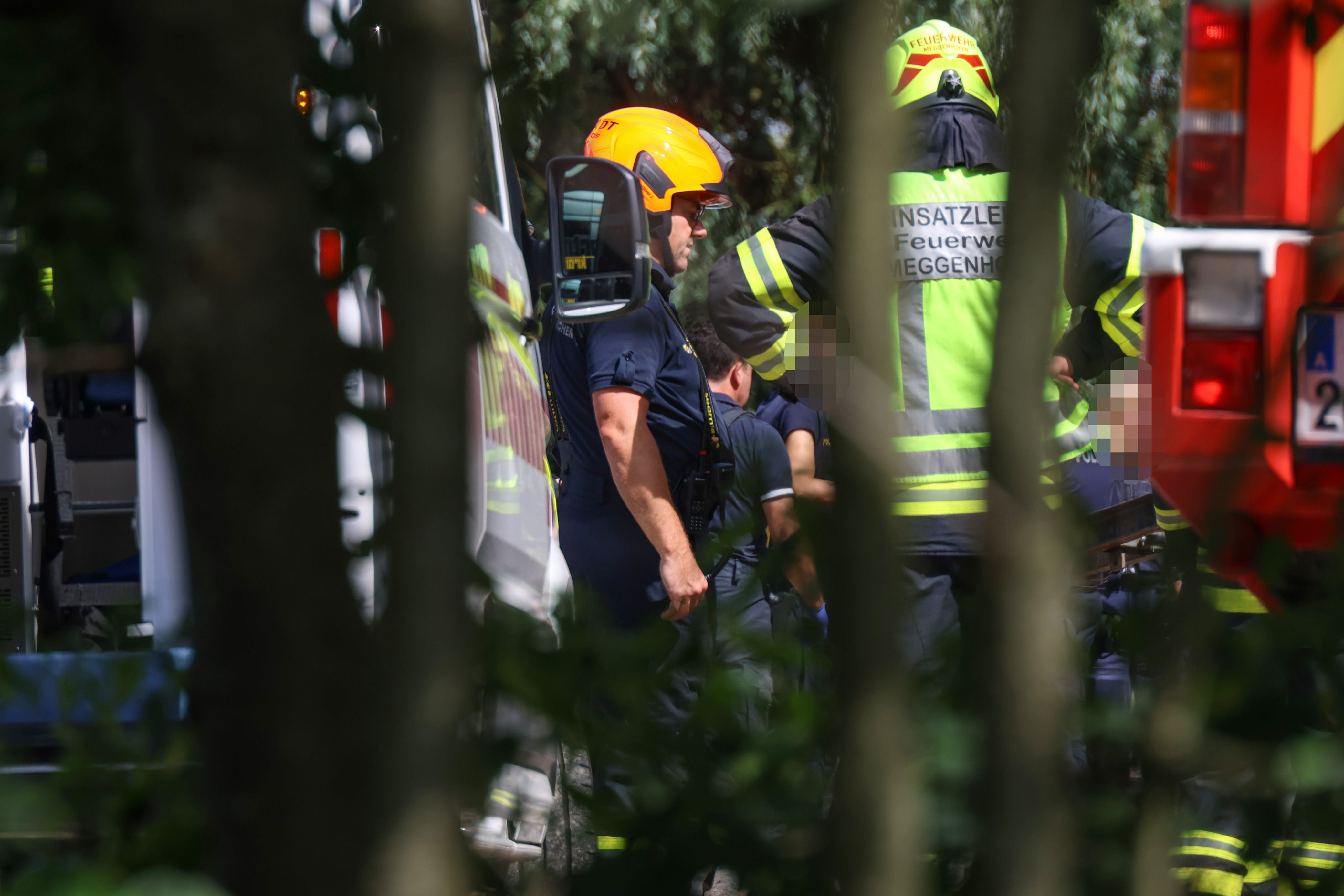 Feuerwehrleute mit Ausrüstung stehen bei einem Einsatz zwischen Einsatzfahrzeugen im Grünen.