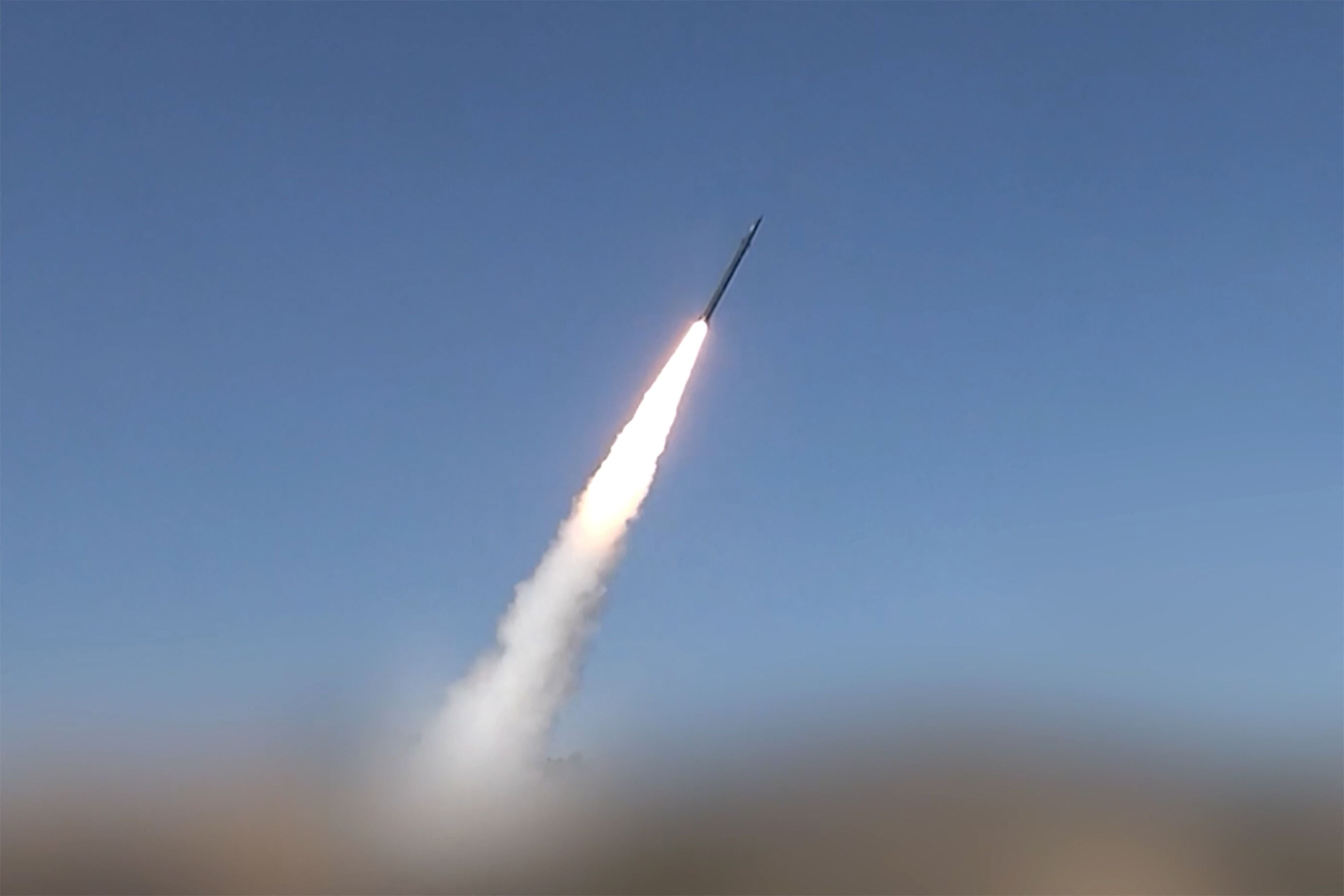 Eine Rakete startet mit Rauchspur in den Himmel vor blauem Hintergrund.