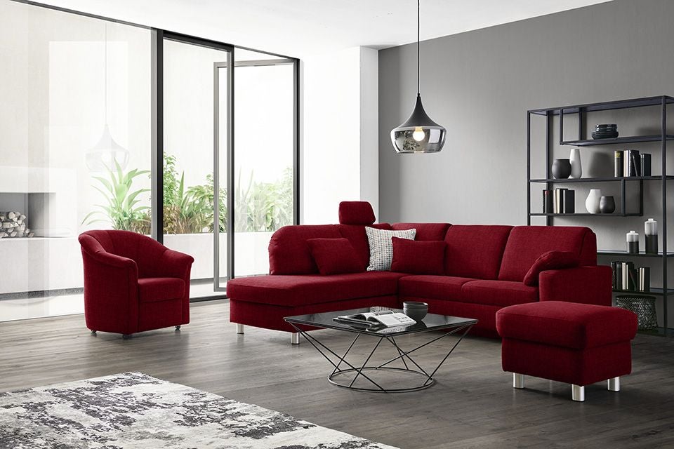 Modernes Wohnzimmer mit rotem Sofa, Sessel, Couchtisch und Regal, helle Fensterfront.