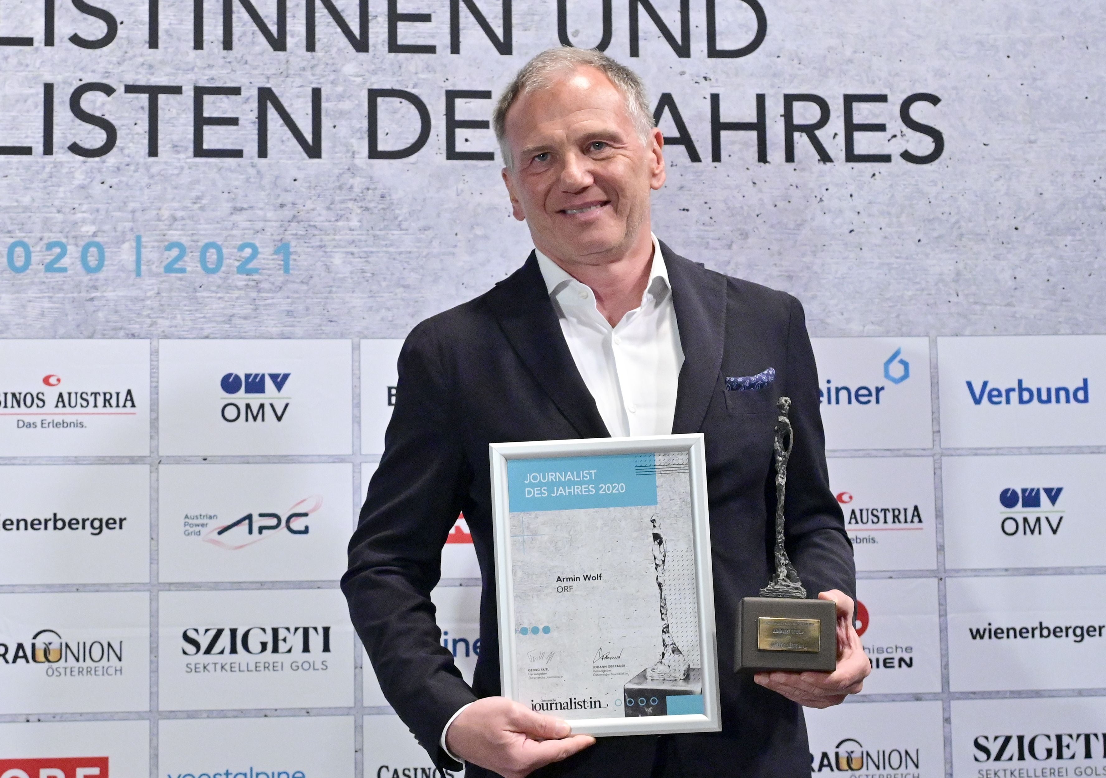 Ein Mann im Anzug hält eine Auszeichnung und eine Urkunde für den "Journalist des Jahres 2020".