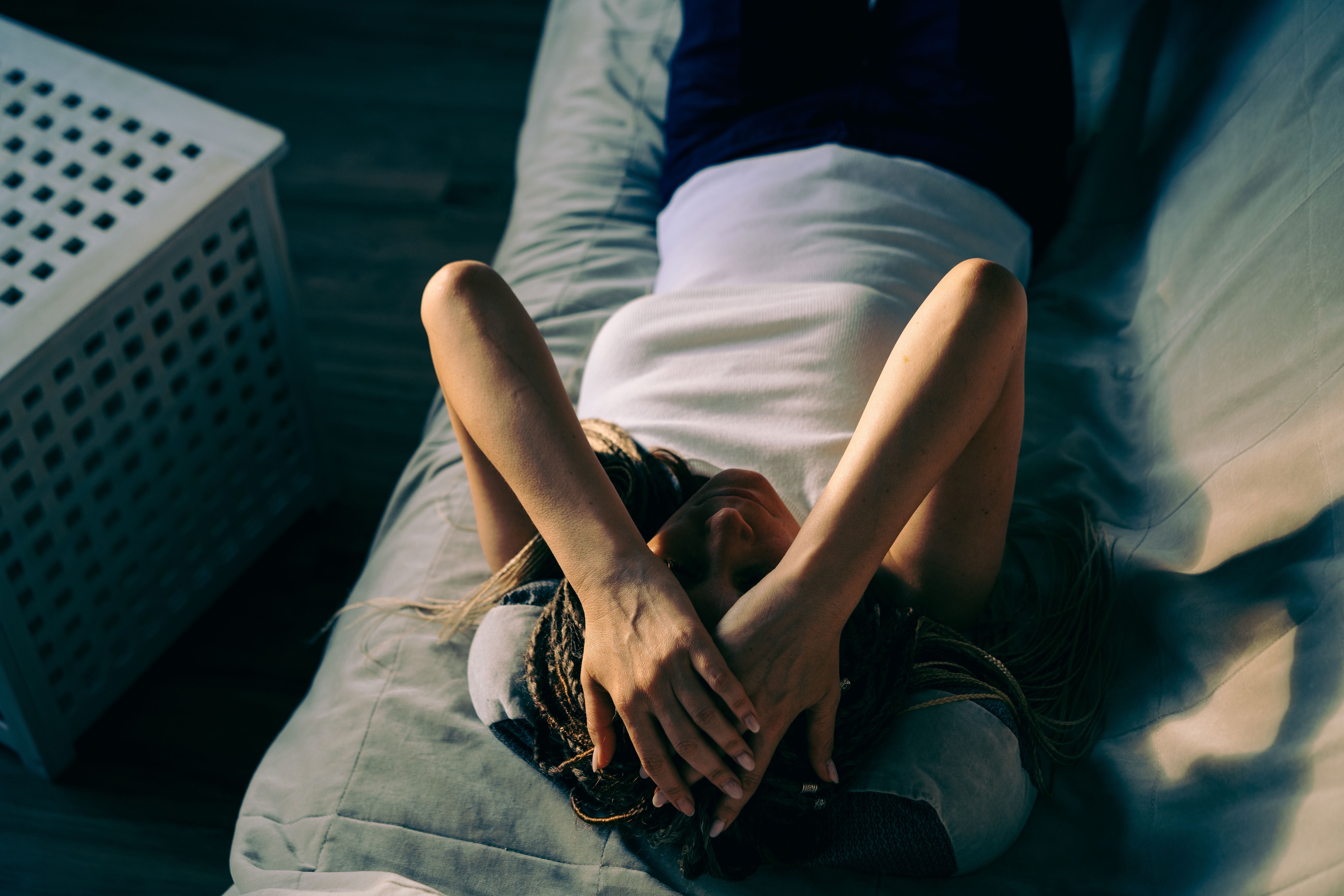 Frau mit Dreadlocks liegt auf dem Sofa und bedeckt ihr Gesicht mit den Händen.