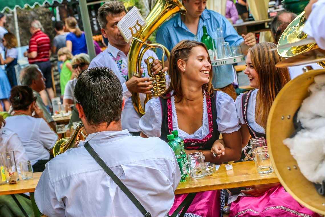 Menschen in Tracht sitzen lachend an einem Tisch mit Blasmusikern beim Neustifter Kirtag.
