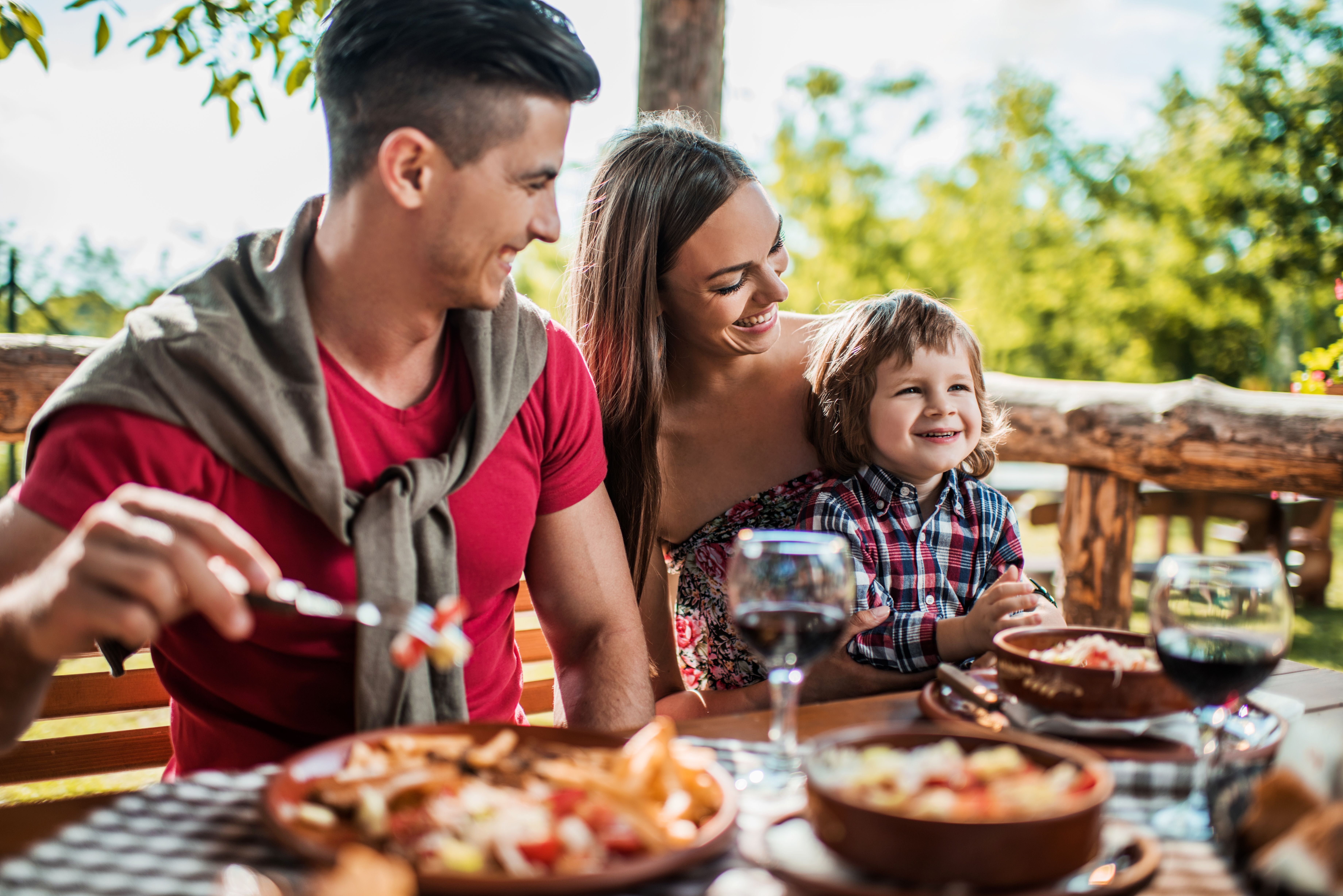 Eine Familie mit kleinem Jungen isst lächelnd auf der Restaurantterrasse im Frühling.
