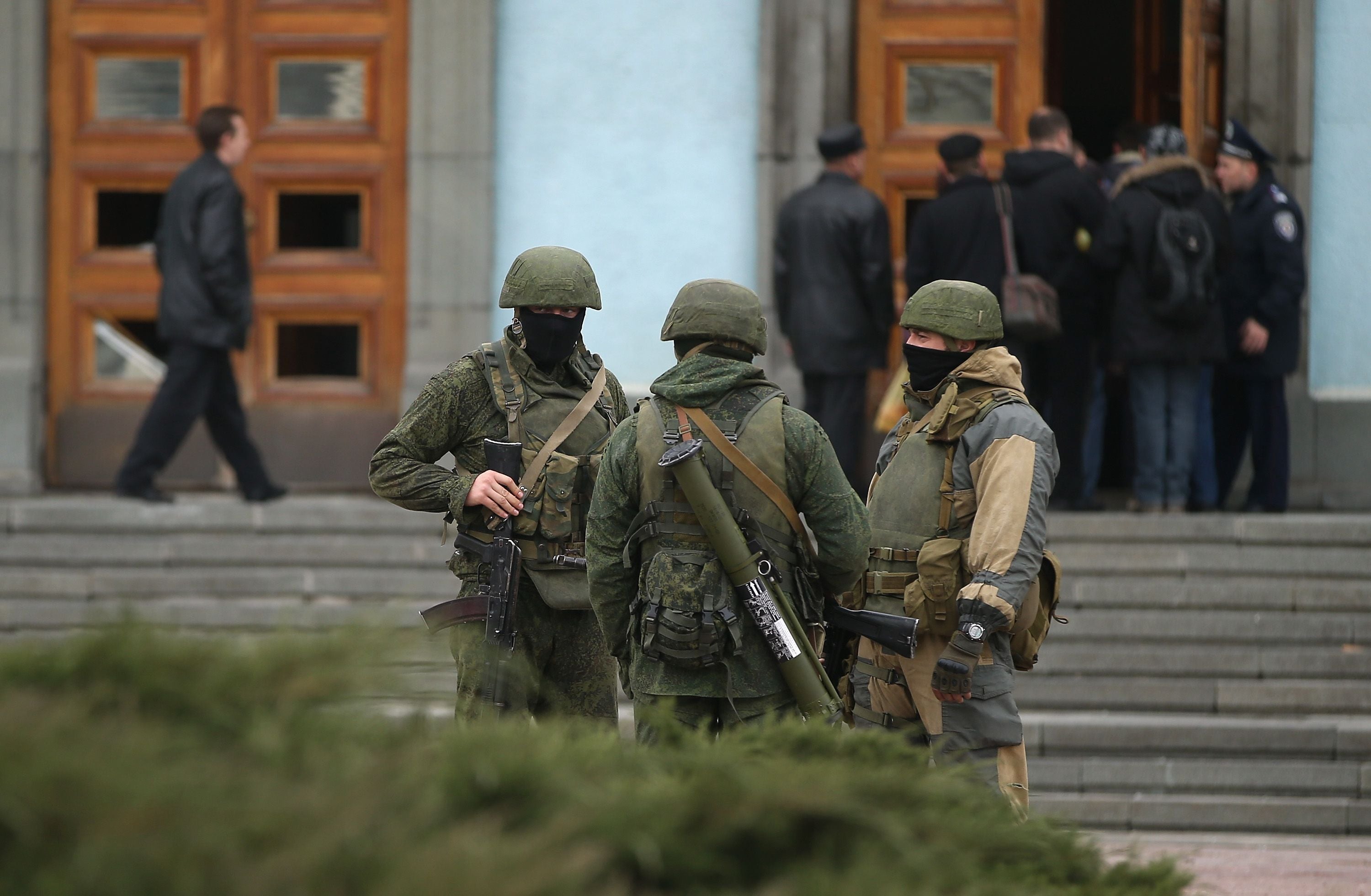 Drei schwerbewaffnete Soldaten ohne Abzeichen stehen vor einem Gebäudeeingang in Simferopol, Ukraine.