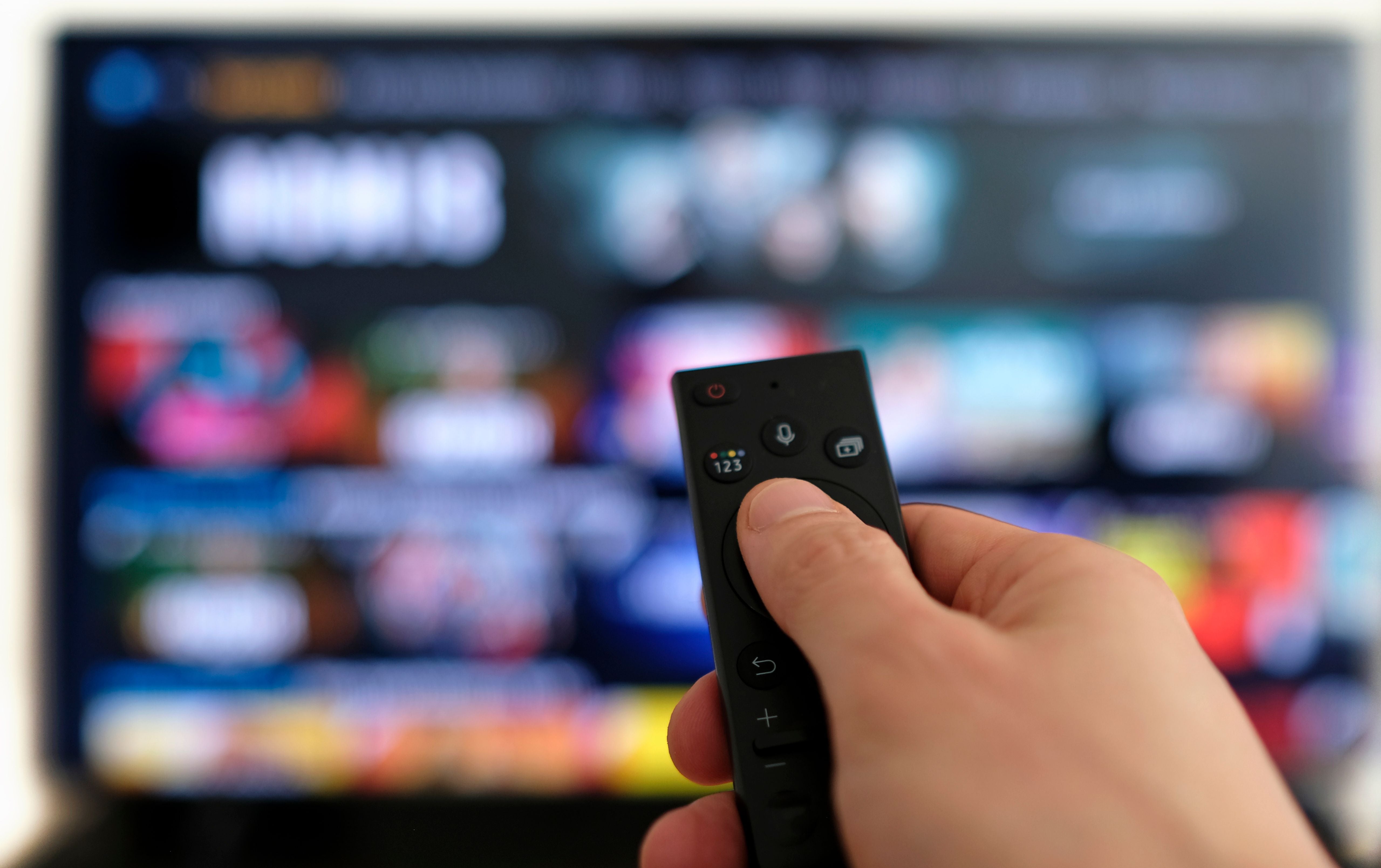 Hand hält Fernbedienung vor einem unscharfen Fernsehbildschirm mit Streaming-Diensten.