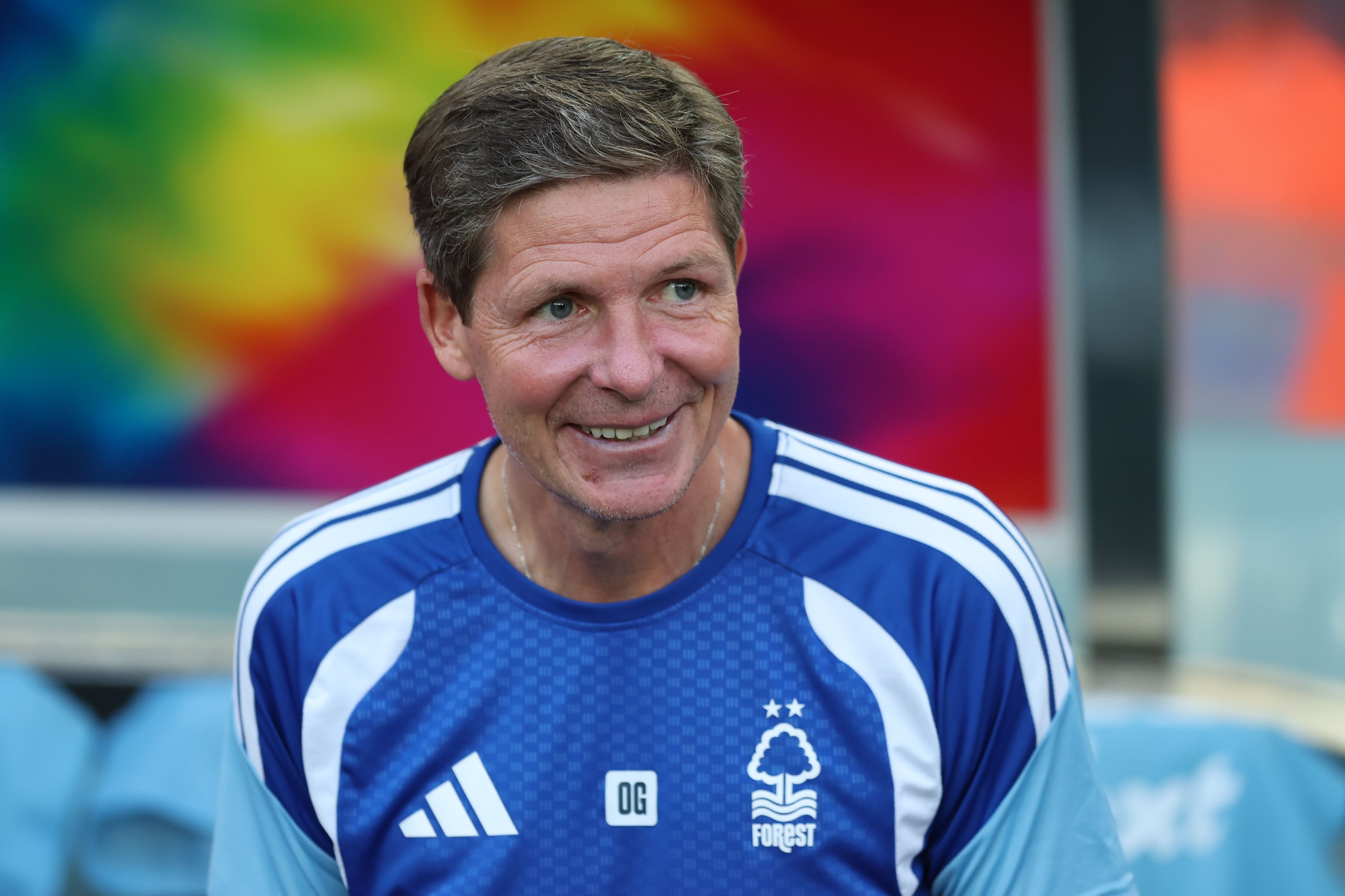 Ein lächelnder Mann im blauen Nottingham-Forest-Trikot sitzt vor buntem Hintergrund.
