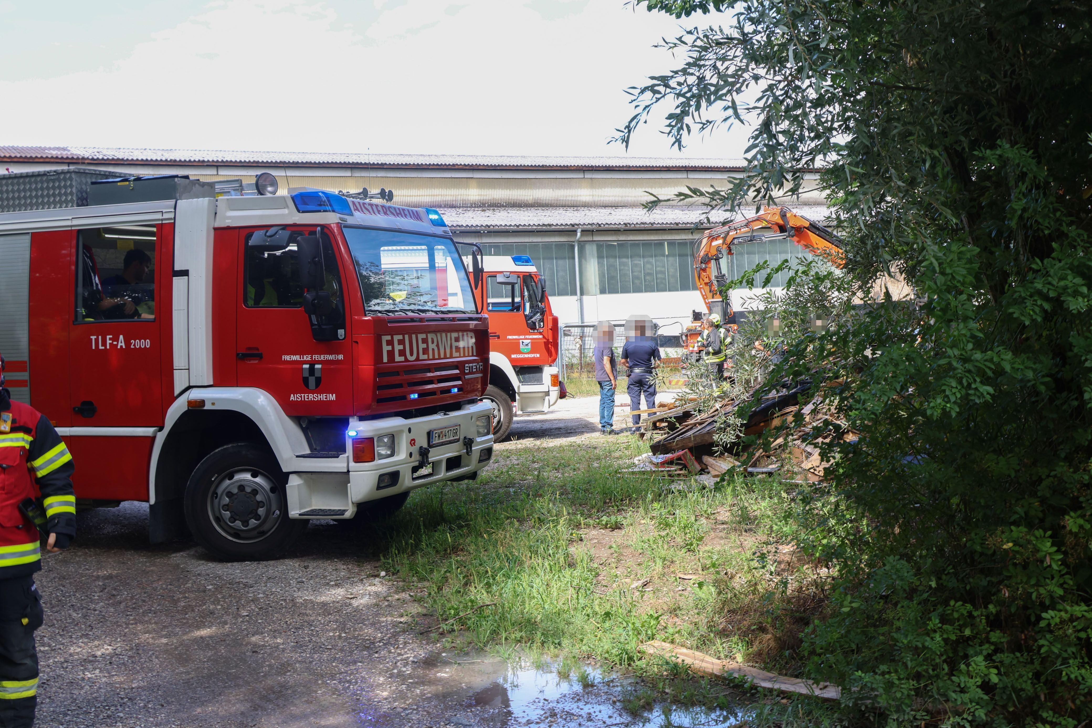 Zwei Feuerwehrfahrzeuge und ein Kran an einem Einsatzort mit Trümmern und Feuerwehrleuten.