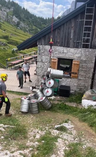 Mehrere Bierfässer hängen an einem Seil und kippen neben einer Berghütte um.