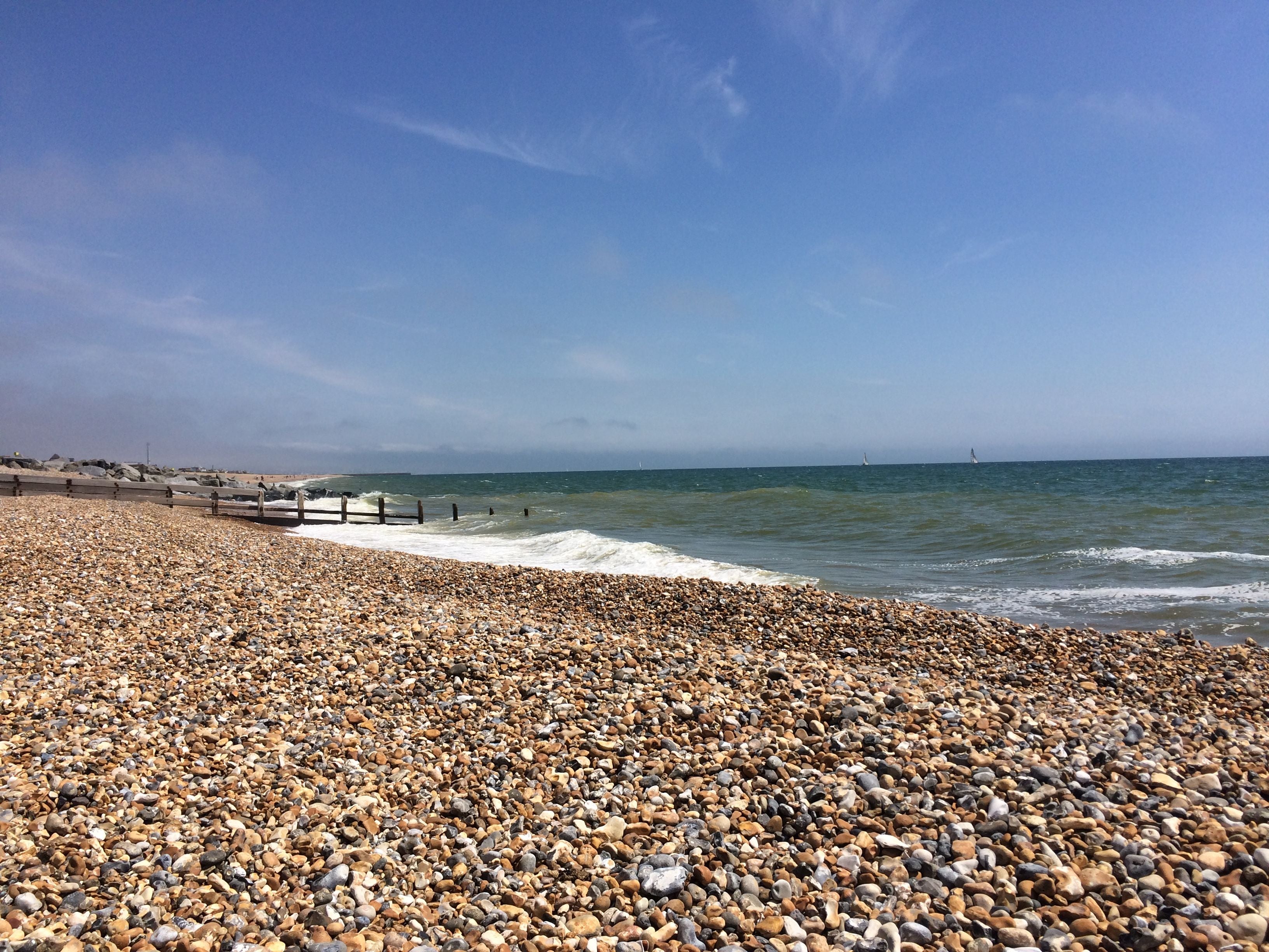 Kieselstrand in Shoreham-by-Sea mit Wellen und blauem Himmel im Hintergrund.