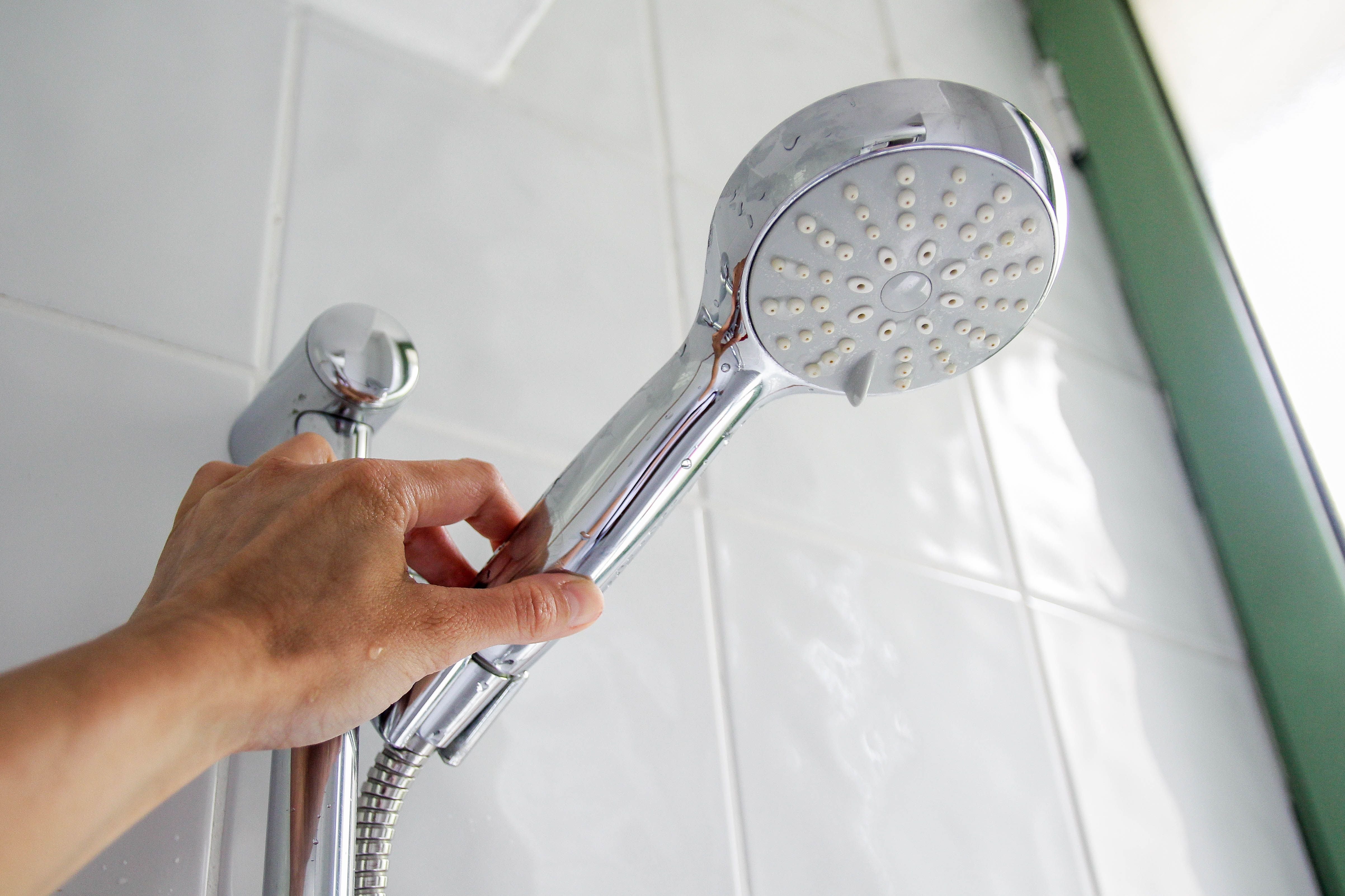 Eine Hand nimmt einen verstellbaren Duschkopf von der Halterung im Badezimmer.