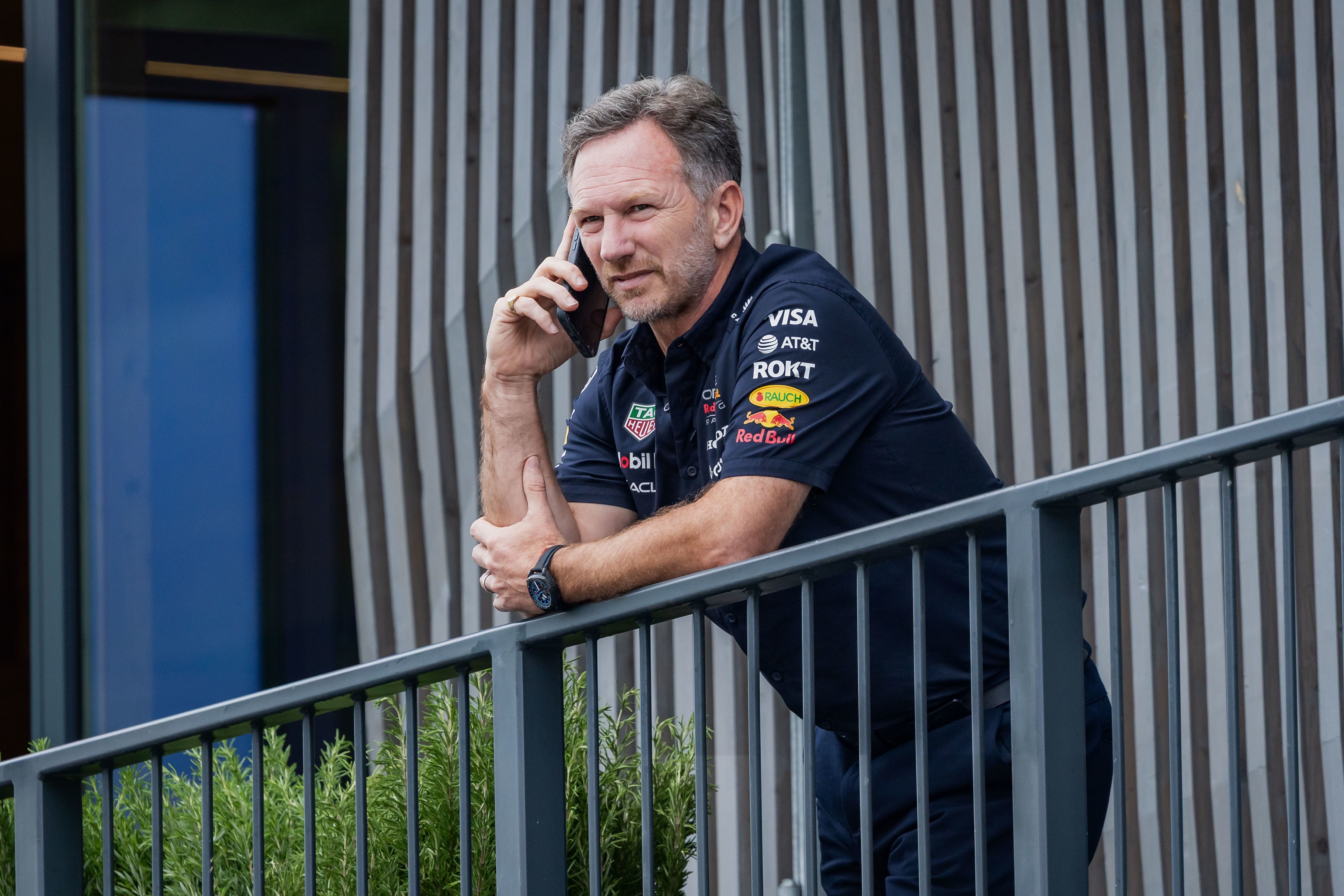 Ein Mann im Red-Bull-Racing-Shirt telefoniert an einem Geländer im Freien.