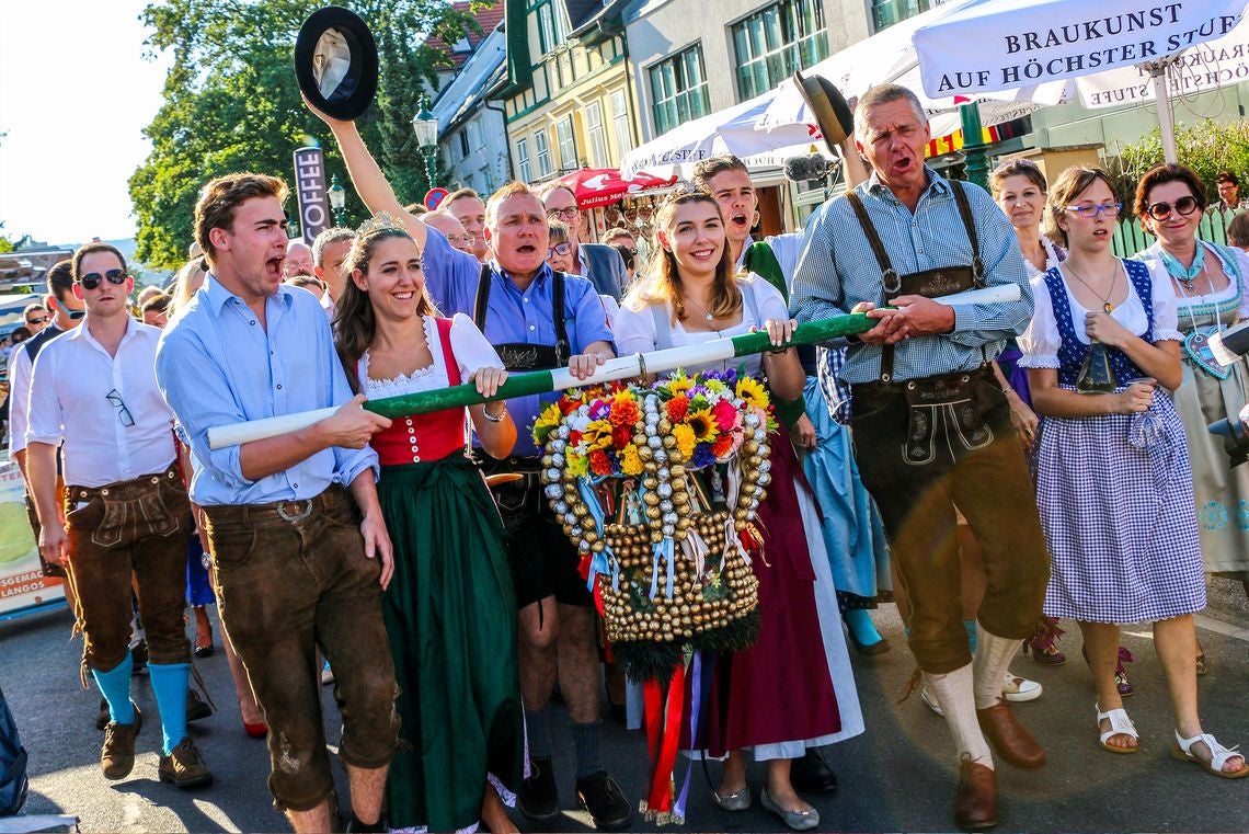 Menschen in Tracht tragen einen geschmückten Kranz beim Neustifter Kirtag durch eine Straße.