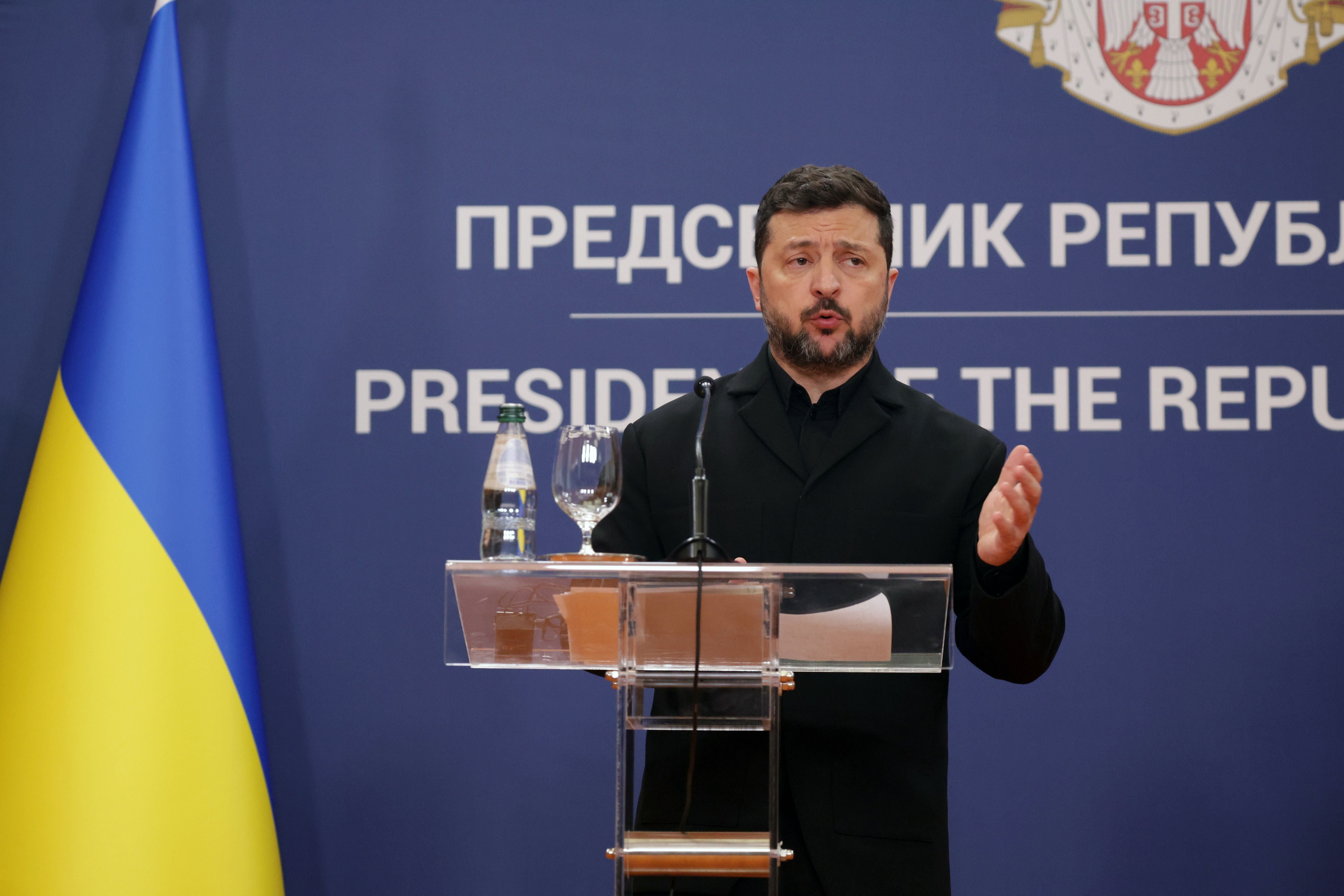 Ein Mann spricht bei einer Pressekonferenz vor einer blauen Wand und einer ukrainischen Flagge.