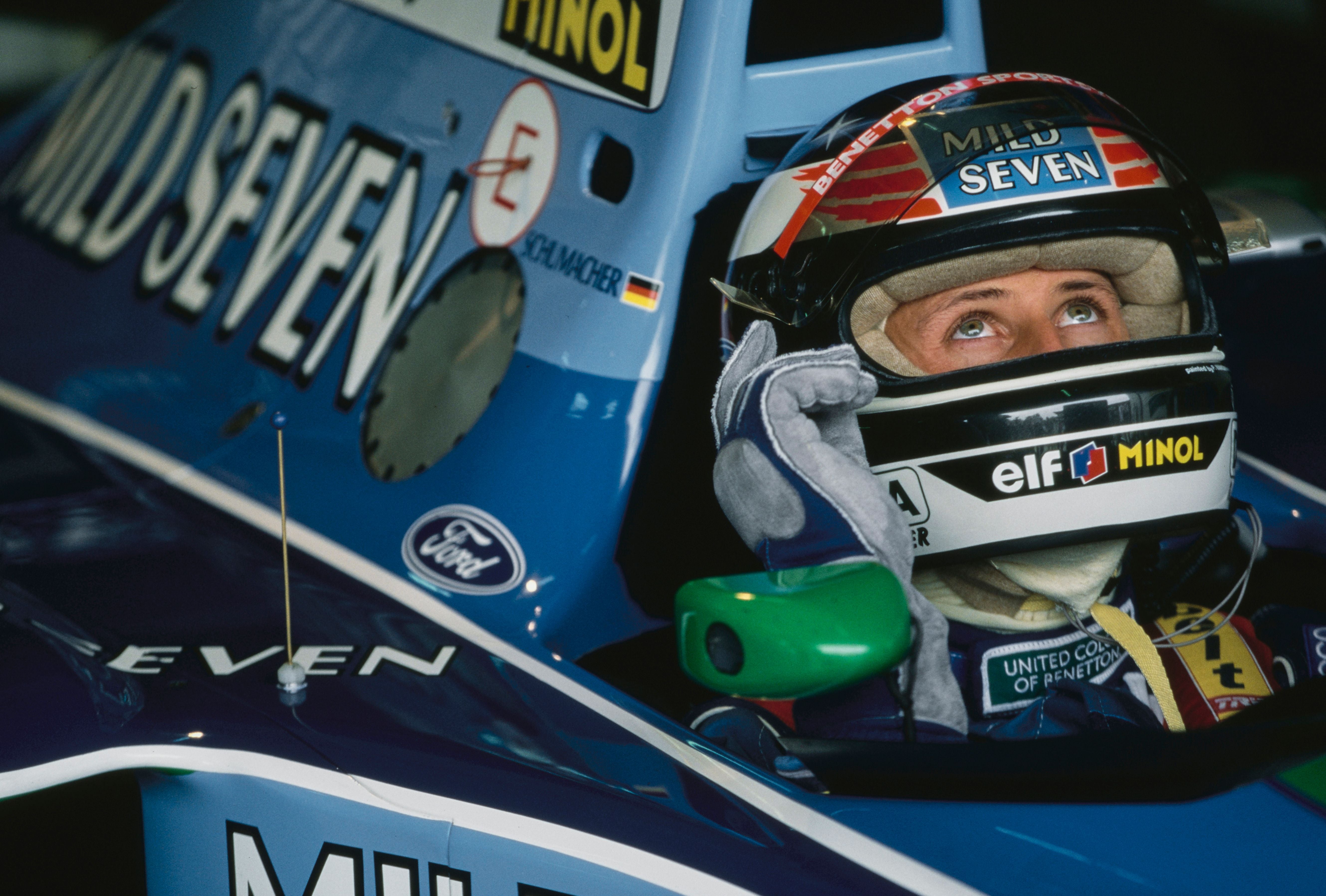 Ein Rennfahrer im blauen Benetton-Formel-1-Auto blickt aus dem Cockpit nach oben.