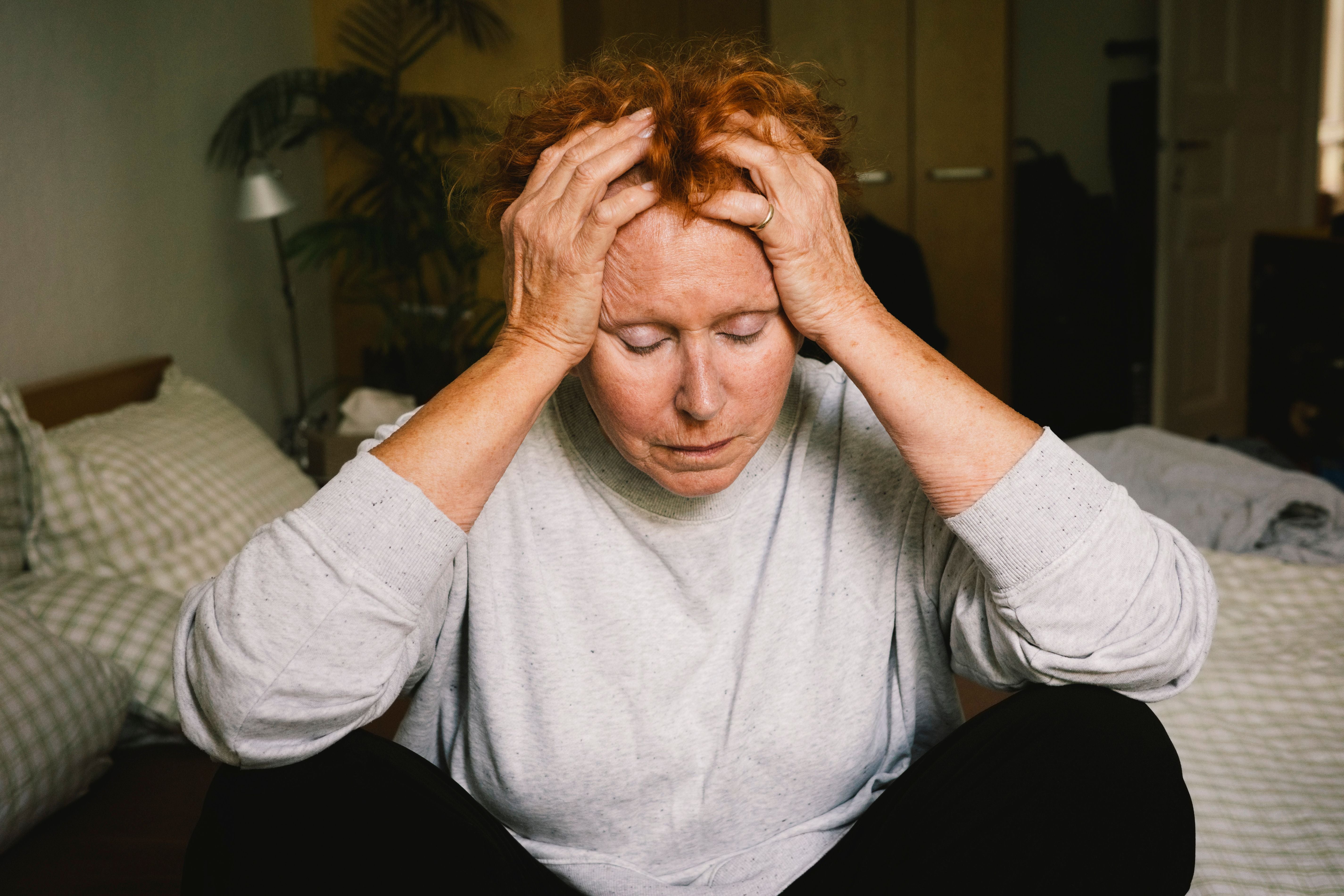 Frau sitzt auf dem Bett und hält gestresst den Kopf in den Händen.
