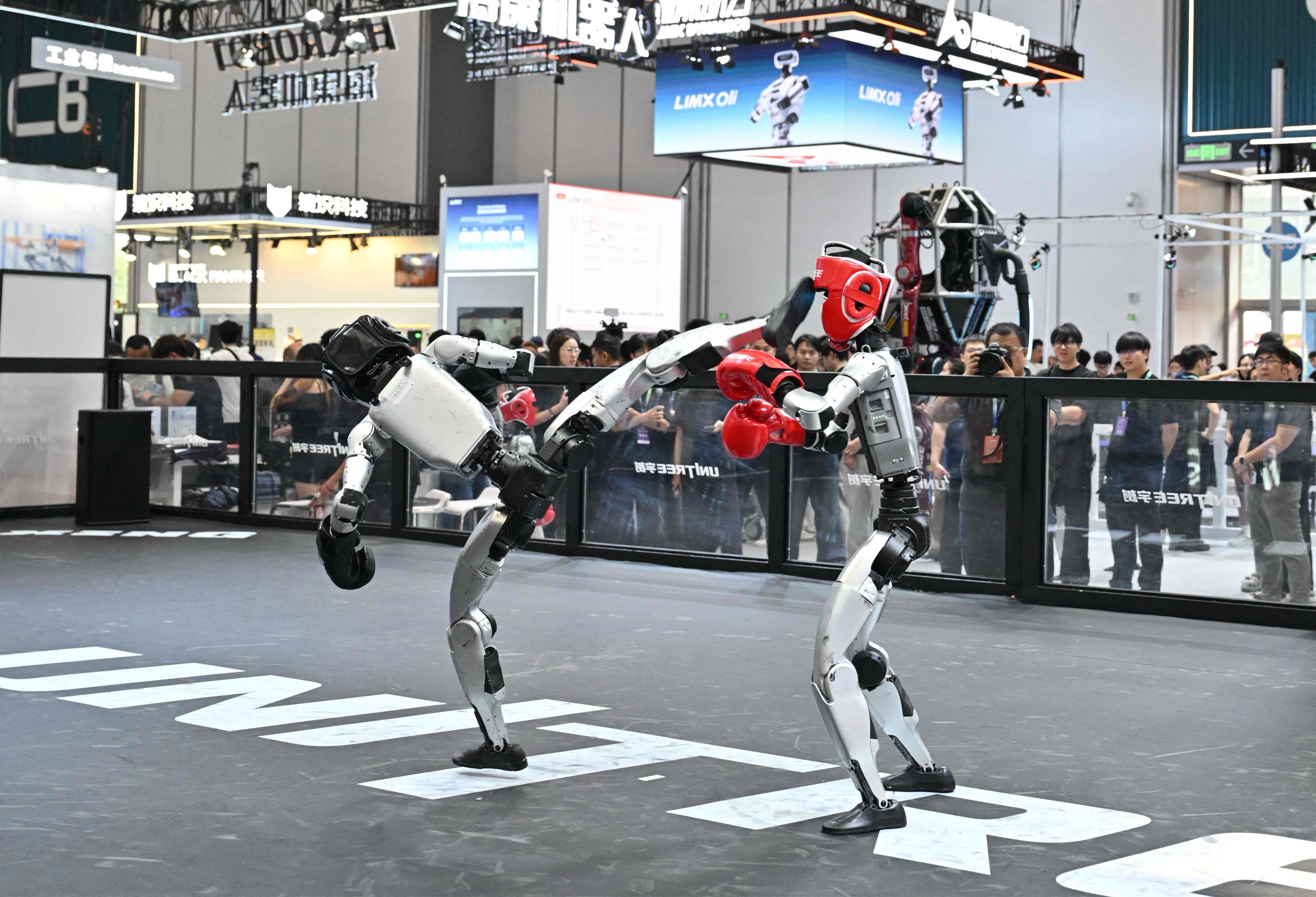 Zwei humanoide Roboter boxen in einem Ring vor Zuschauern auf einer Messe.