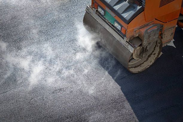 Straßenwalze verdichtet heißen Asphalt, Dampf steigt bei der Straßenreparatur auf.