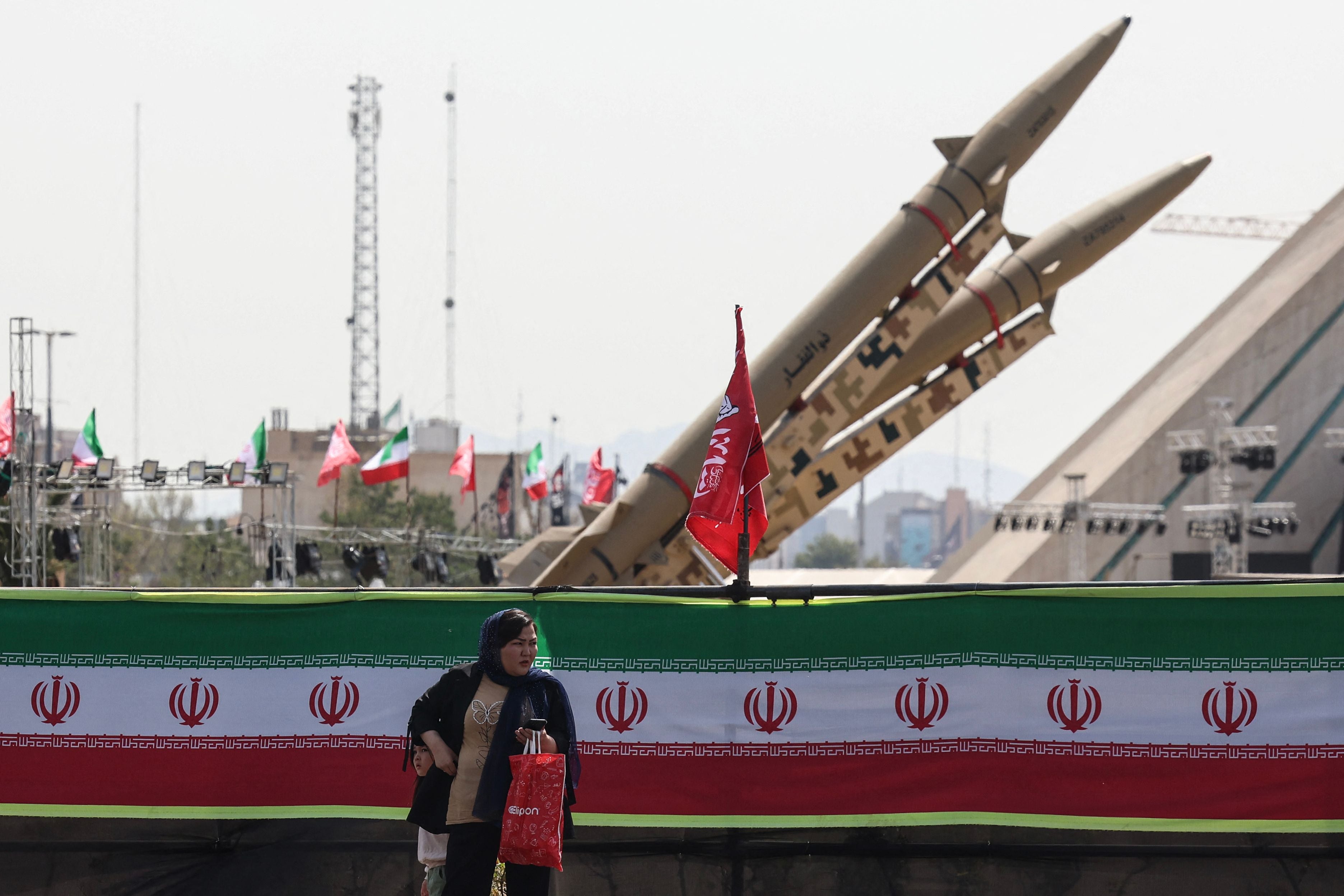 Eine Frau steht vor iranischen Zolfaghar-Raketen auf einem Platz mit iranischer Flagge.