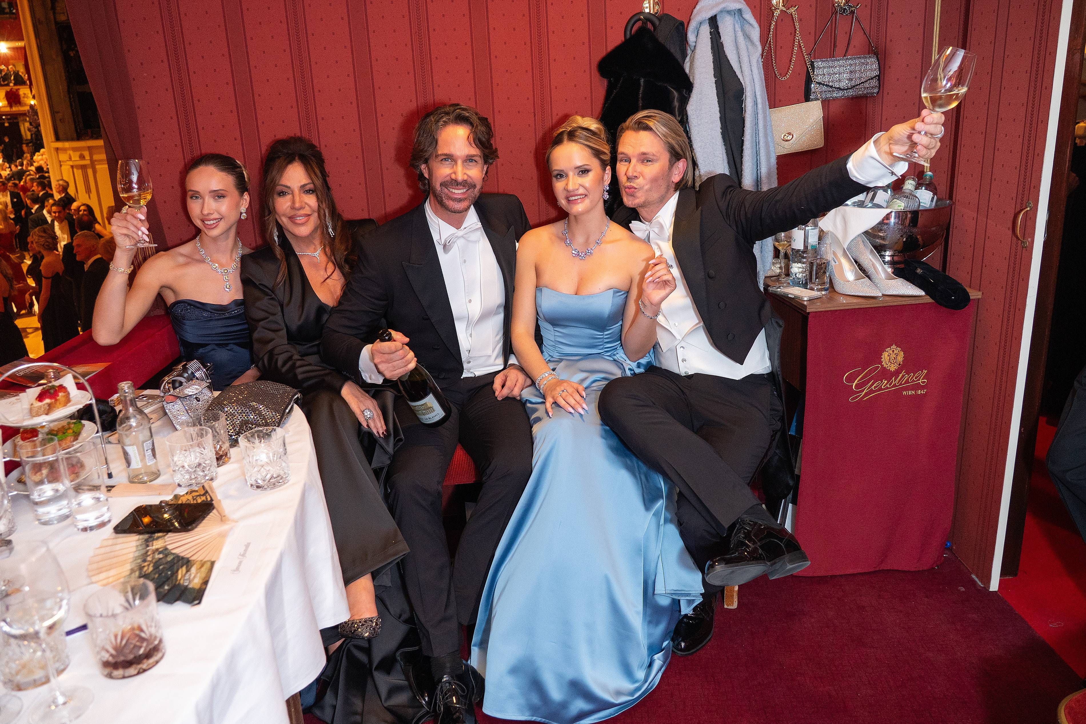 Fünf elegant gekleidete Personen feiern mit Getränken in einer Loge beim Wiener Opernball.