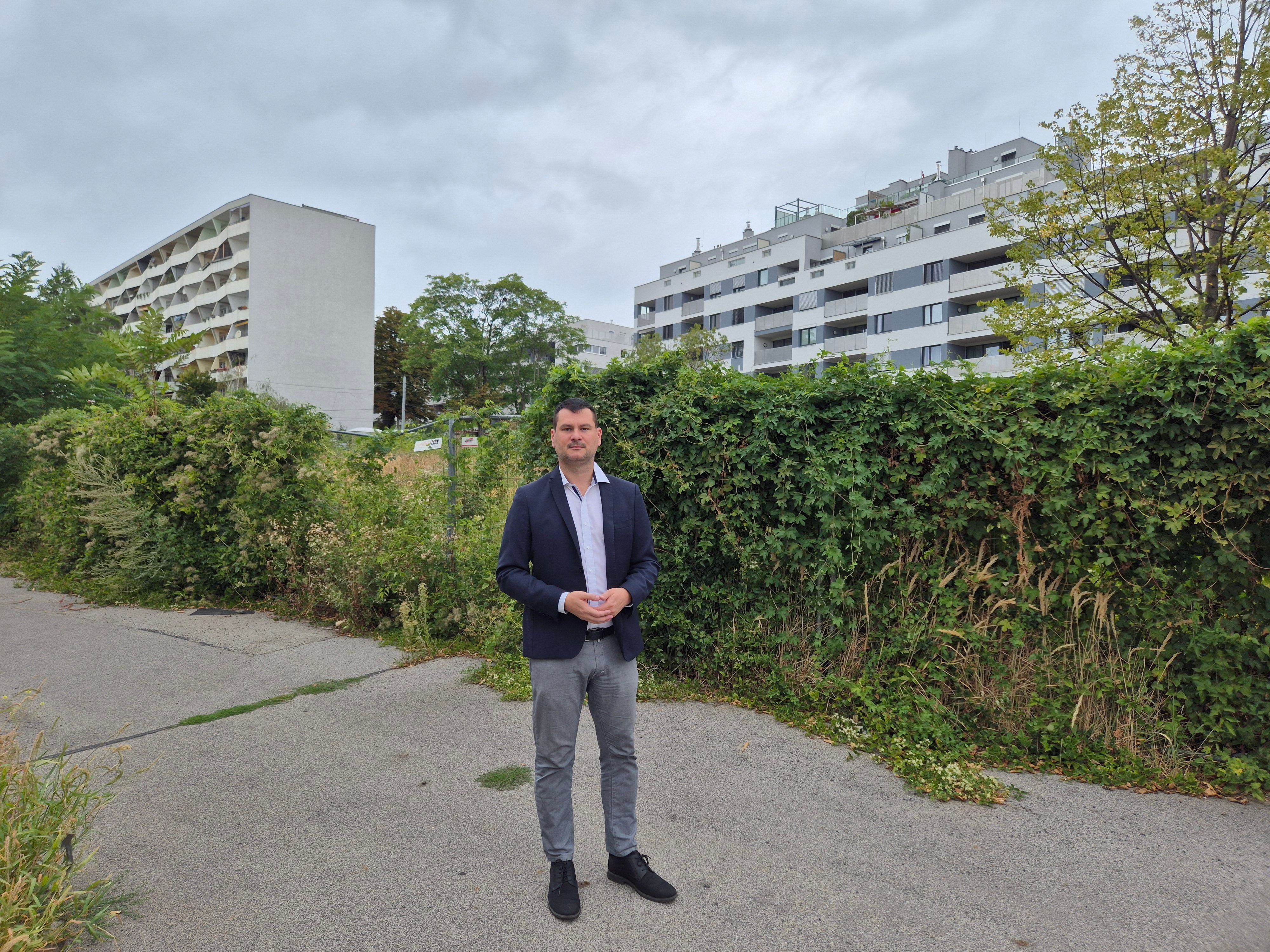 Ein Mann im Anzug steht im Kendlerpark in Penzing vor Büschen und Wohnhäusern.
