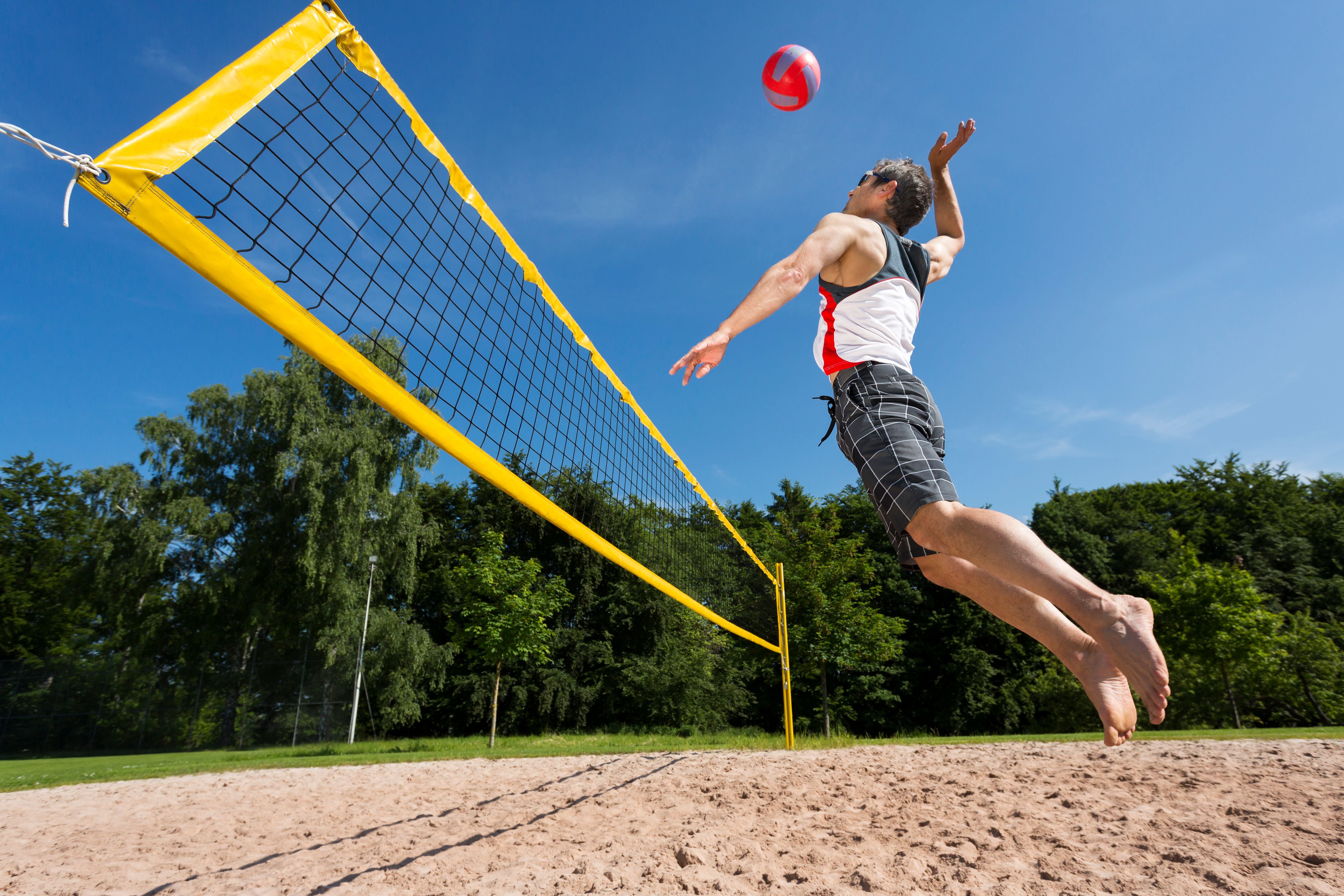 Ein Mann springt beim Beachvolleyball draußen zum Ball und bereitet einen Schlag vor.