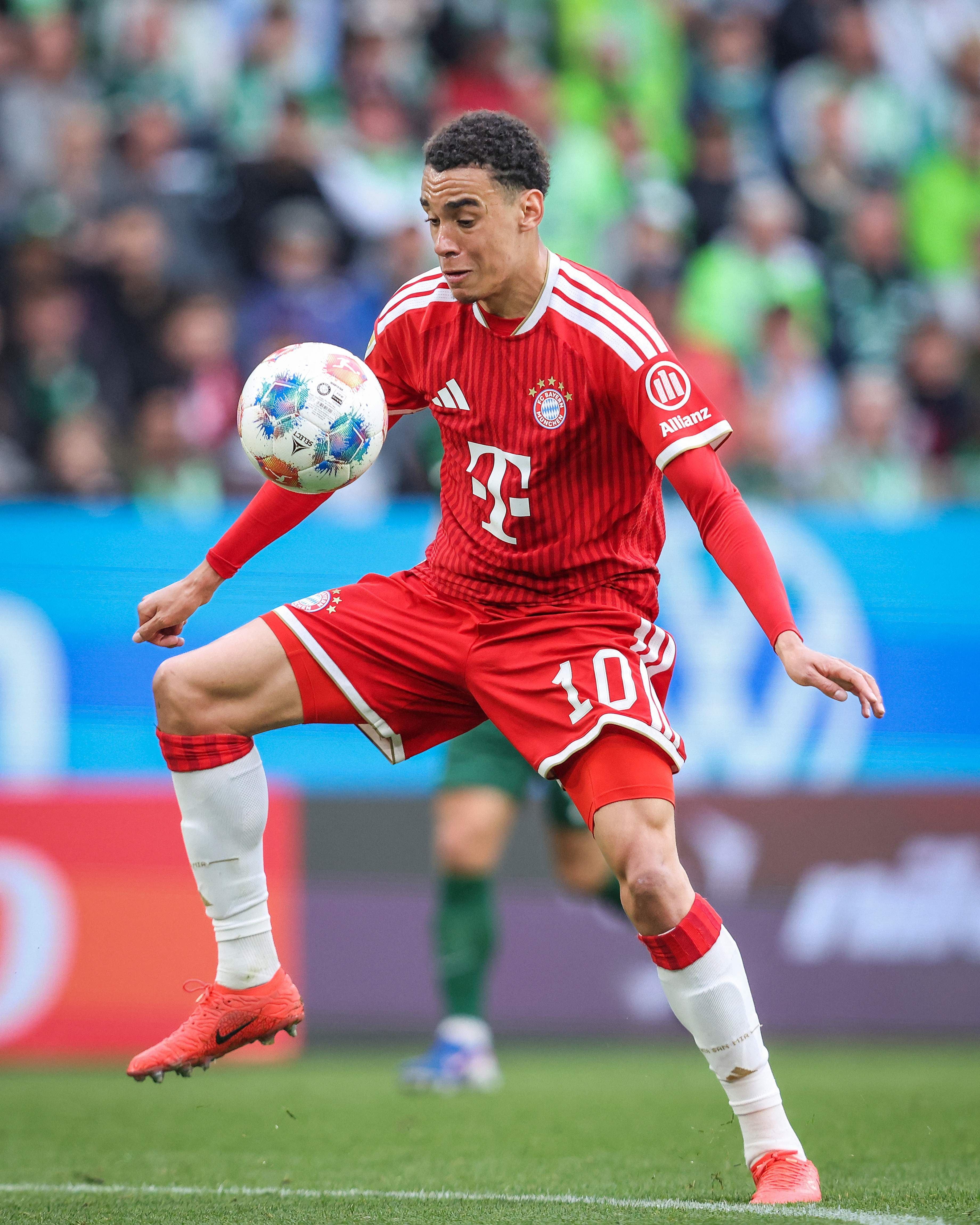 Ein Bayern-Spieler im roten Trikot kontrolliert den Fußball während eines Spiels auf dem Spielfeld.