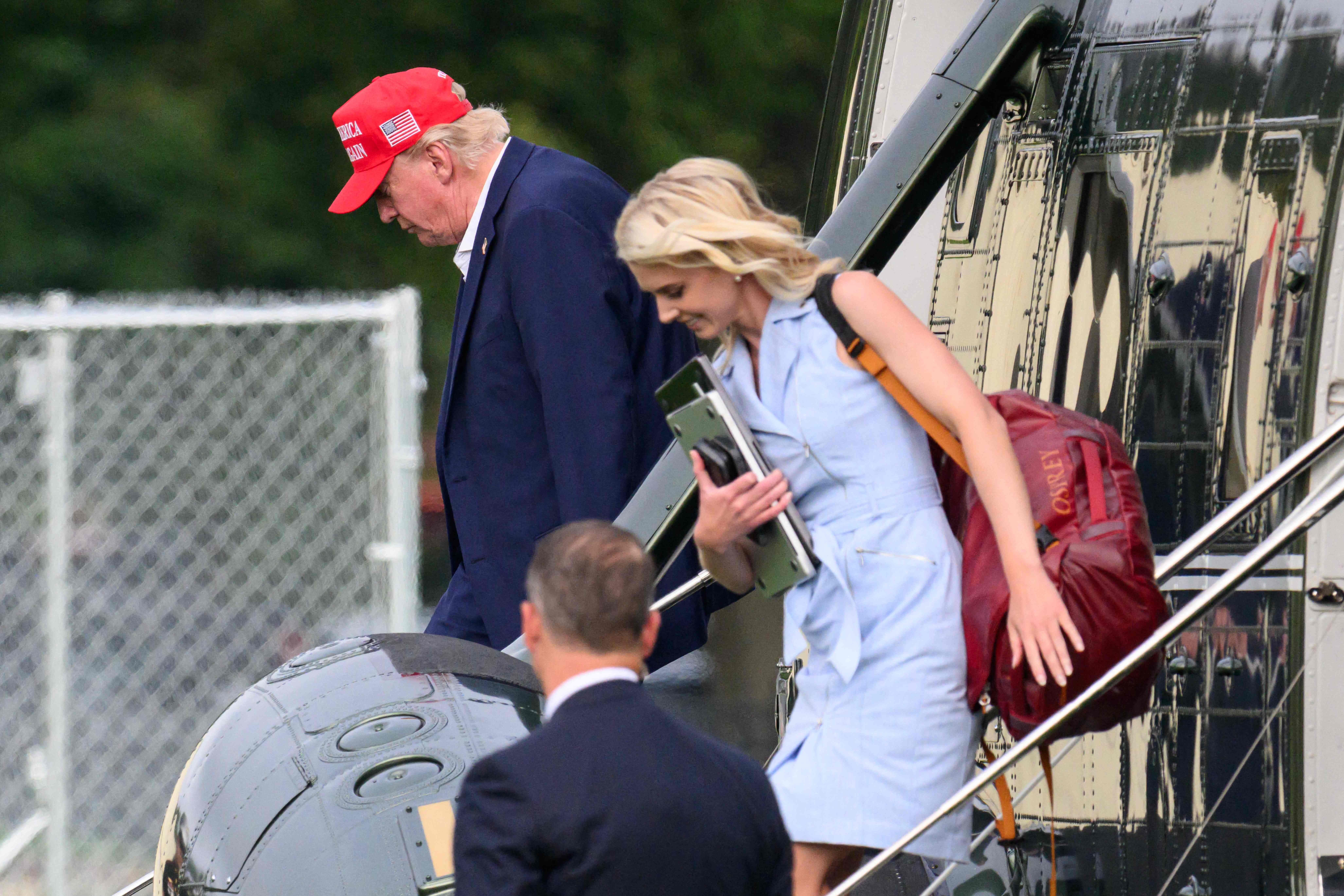 Ein Mann mit roter Mütze und eine Frau steigen aus einem Hubschrauber mit Reflexionen am Rumpf.