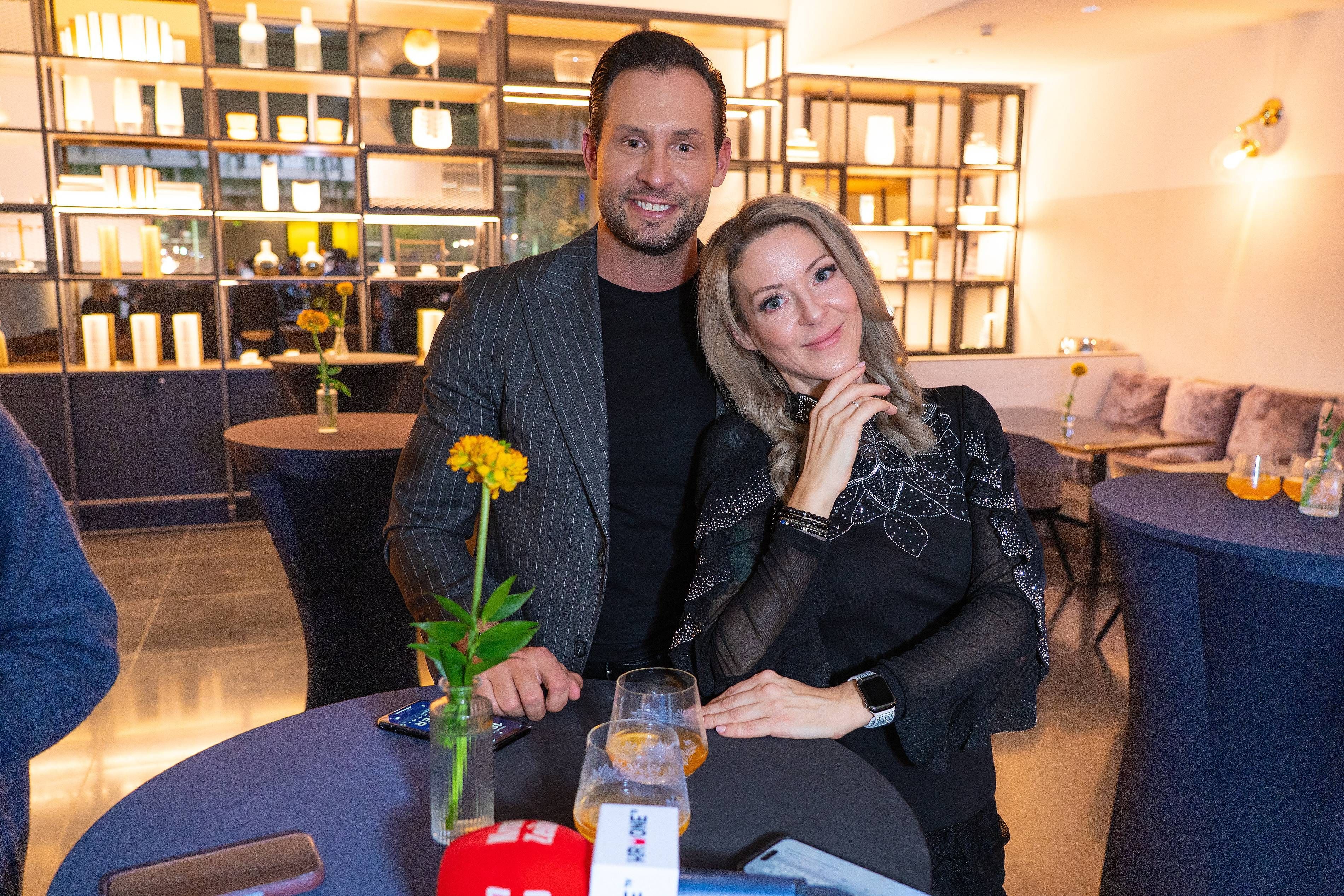 Ein Mann und eine Frau posieren lächelnd an einem Bartisch in modernem, stilvollem Ambiente.