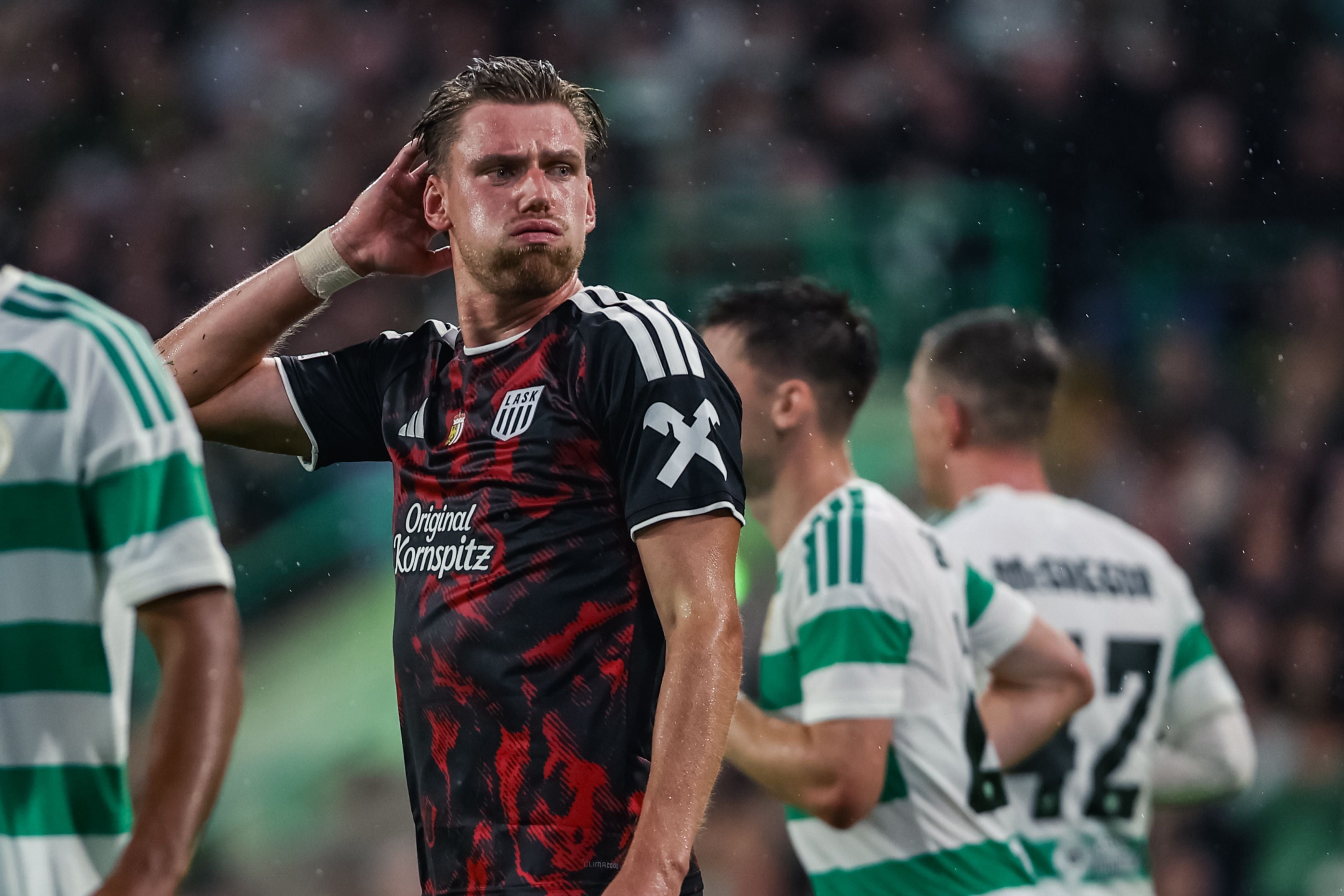 Ein Fußballspieler von LASK steht nachdenklich auf dem Spielfeld, im Hintergrund Gegenspieler.
