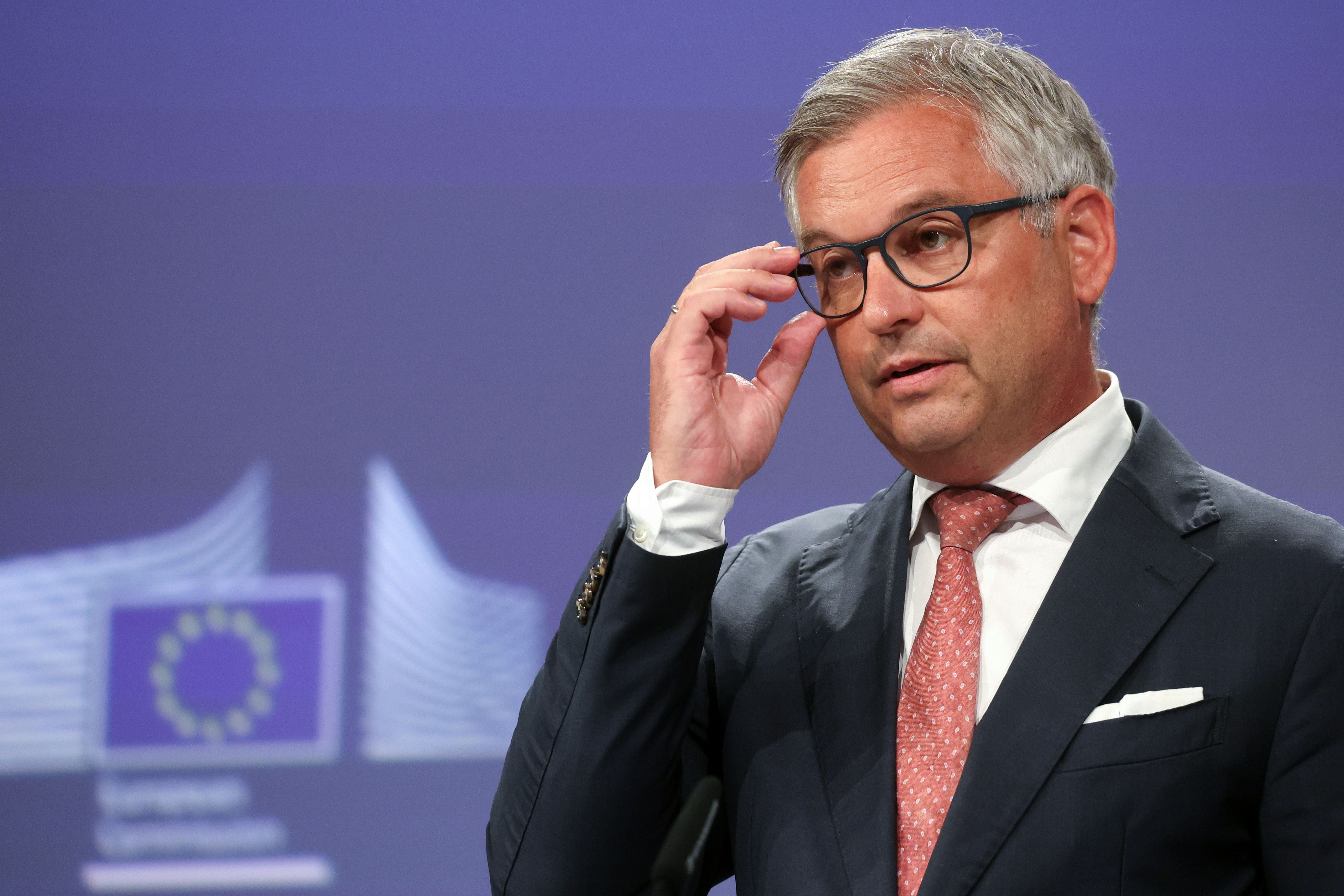 Ein Mann im Anzug spricht während einer Pressekonferenz vor EU-Logos und hält seine Brille fest.