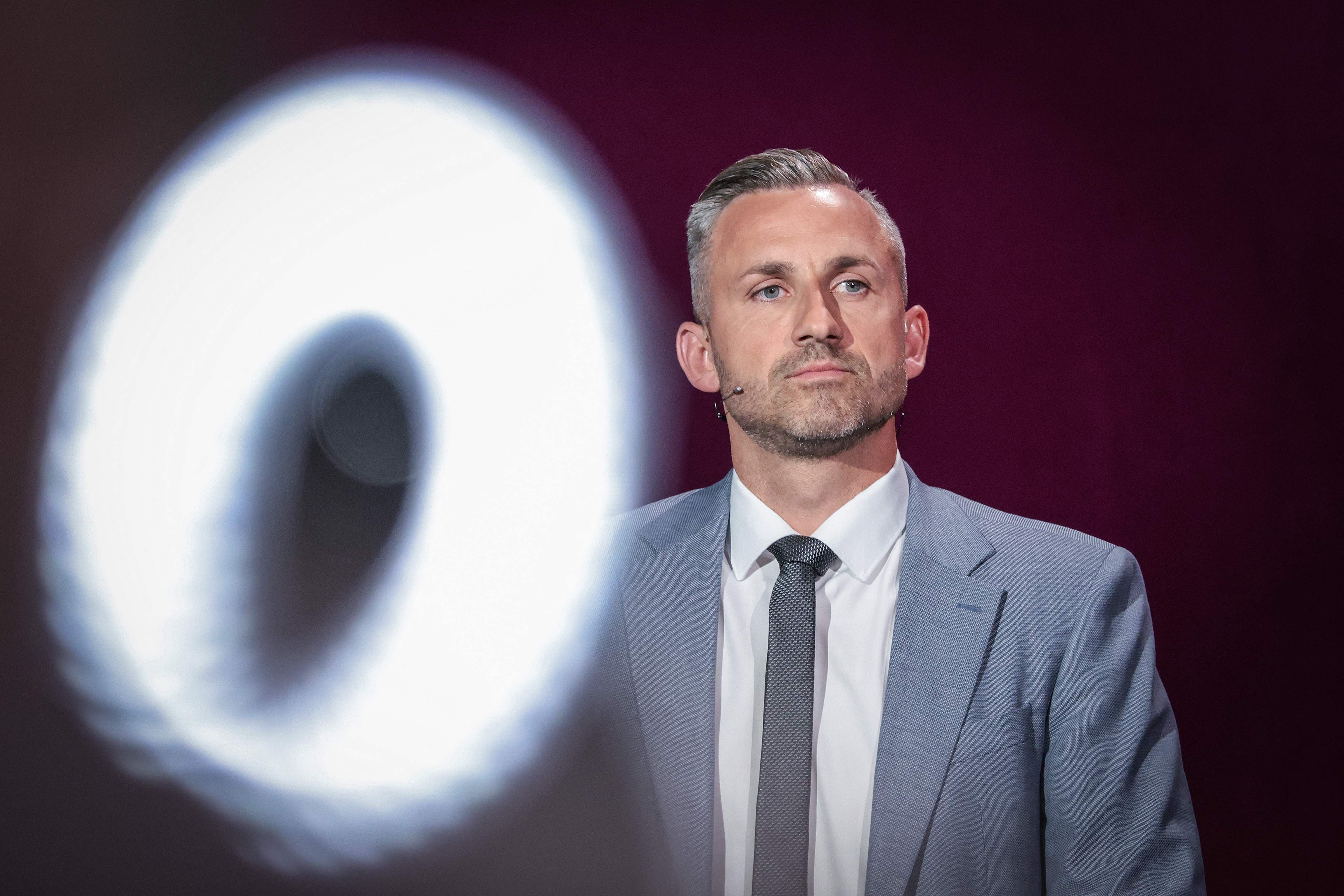 Ein Mann im Anzug bei einer TV-Debatte, im Vordergrund ein unscharfer heller Kreis.