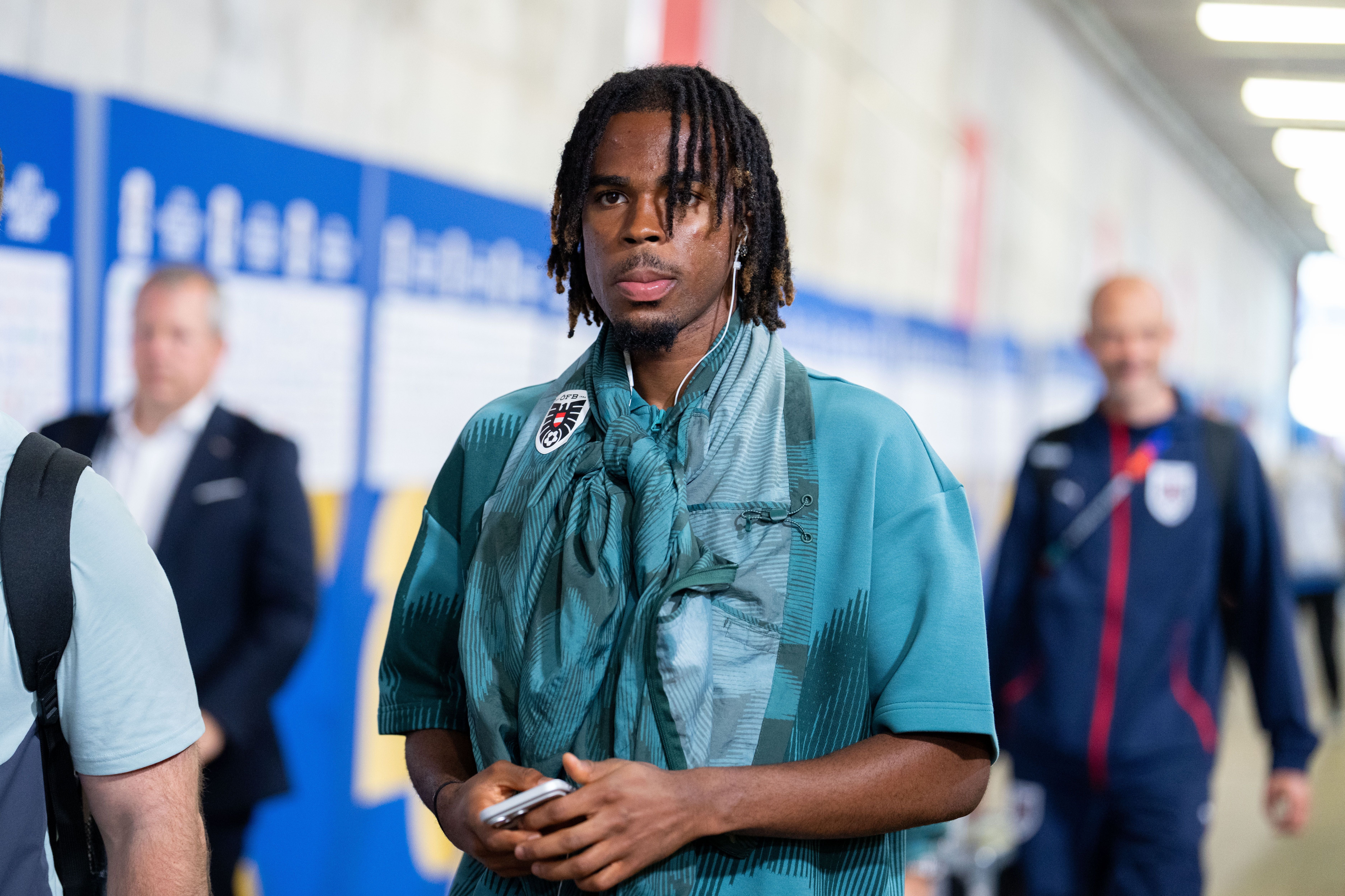 Ein Fußballspieler mit Dreadlocks trägt Trainingsanzug und Kopfhörer beim Stadionankunft.