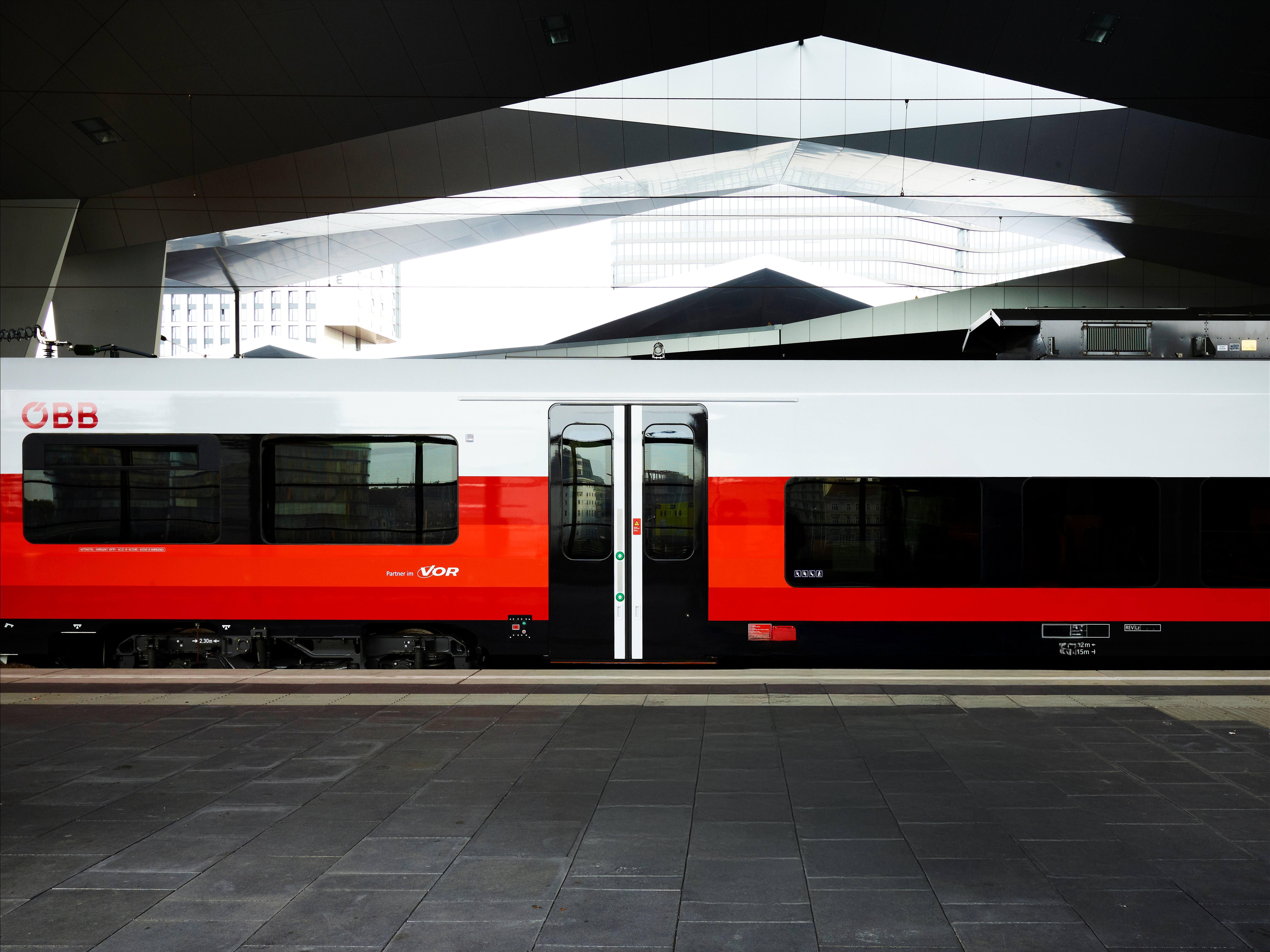 Ein rot-weißer ÖBB-Zug steht an einem modernen Bahnsteig mit überdachtem Bahnhof.