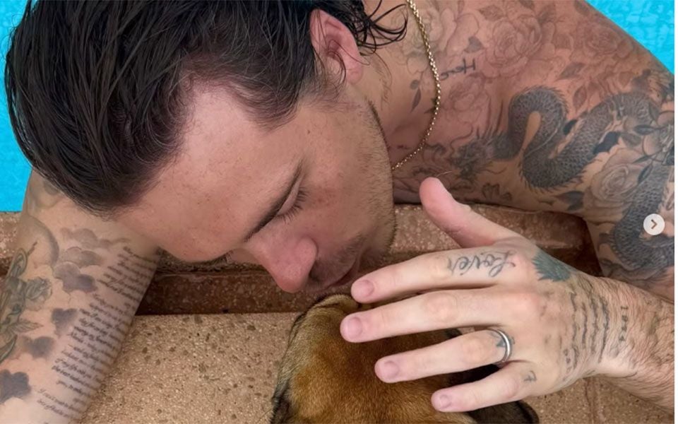 Ein tätowierter Mann küsst einen Hund am Rand eines Pools.