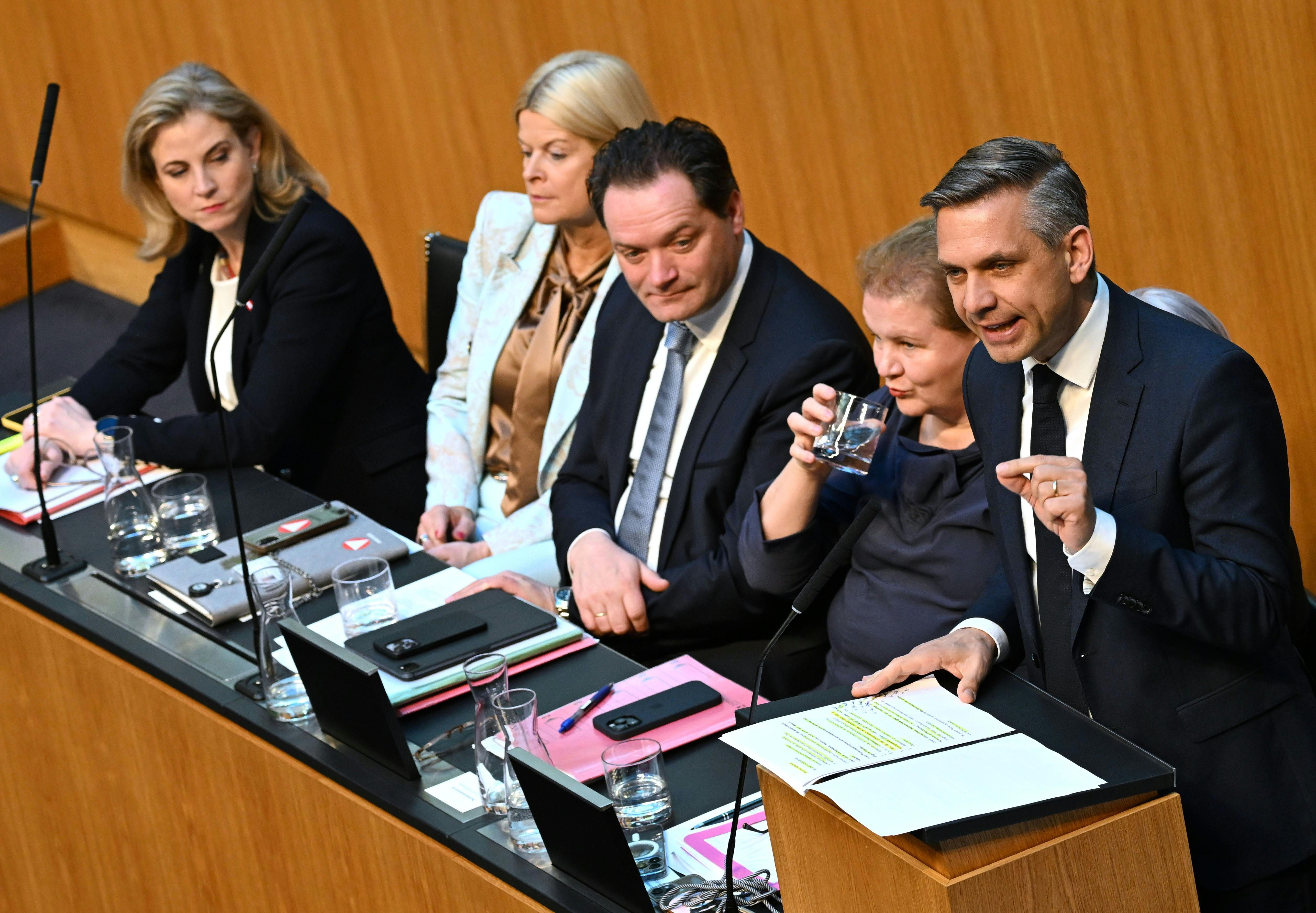 Fünf Politiker sitzen am Tisch im Nationalrat, einer spricht am Rednerpult, andere hören zu.