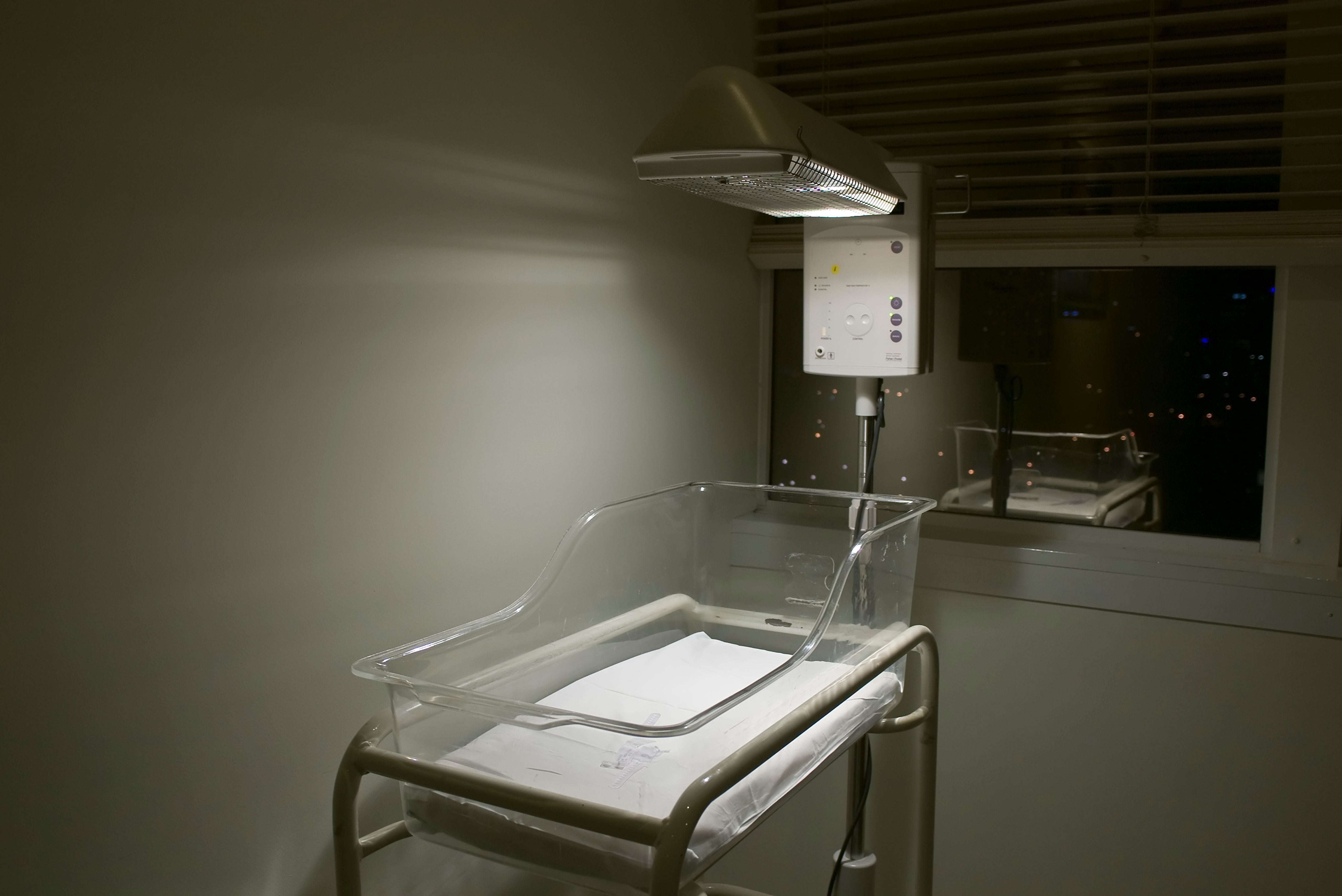 Leeres Babybett mit Wärmelampe in einem Krankenhauszimmer bei Nacht.