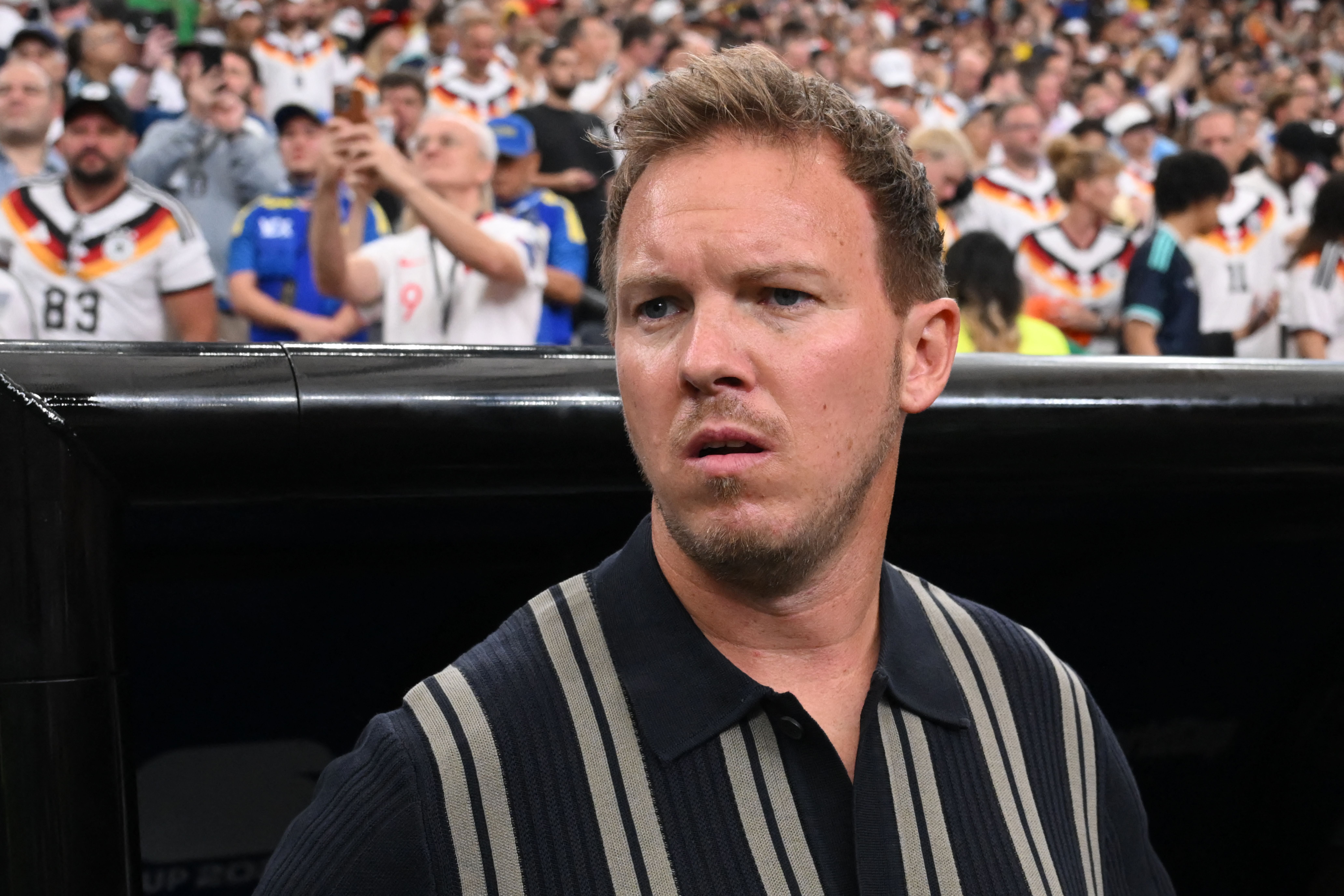 Julian Nagelsmann im Stadion vor einem Fußballspiel, Fans im Hintergrund.
