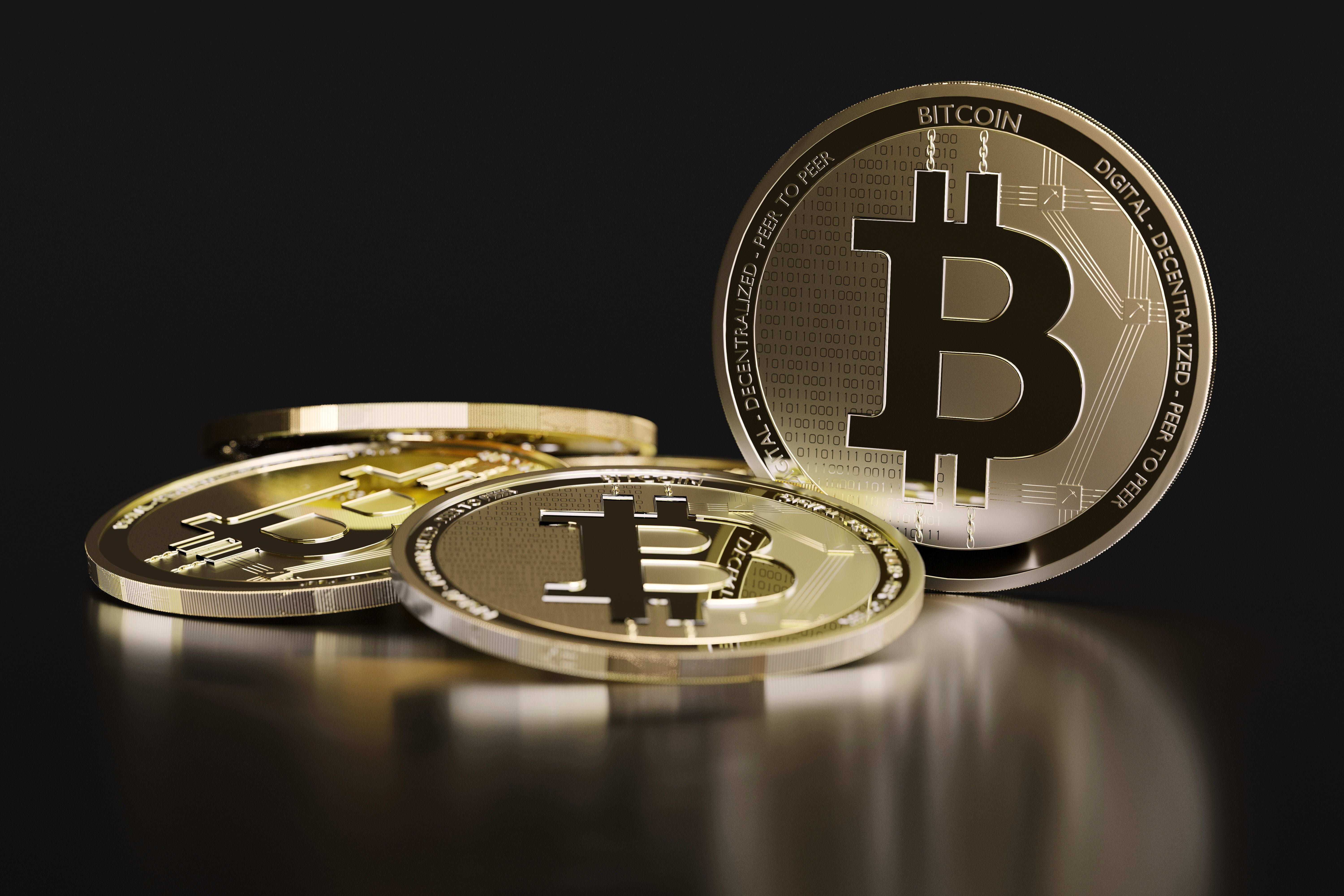 Mehrere goldene Bitcoin-Münzen liegen auf einer reflektierenden, dunklen Oberfläche.