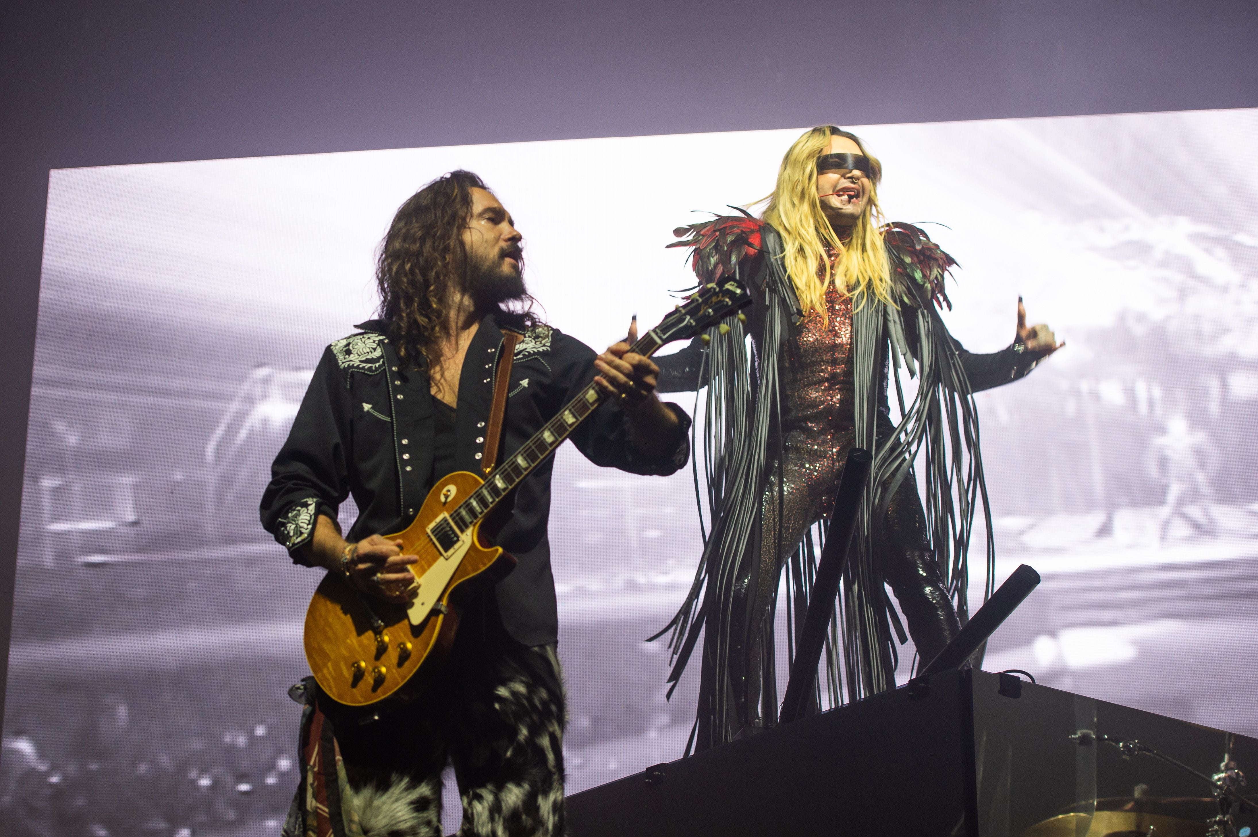 Zwei Musiker von Tokio Hotel treten mit Gitarre und auffälligem Kostüm auf einer Bühne auf.