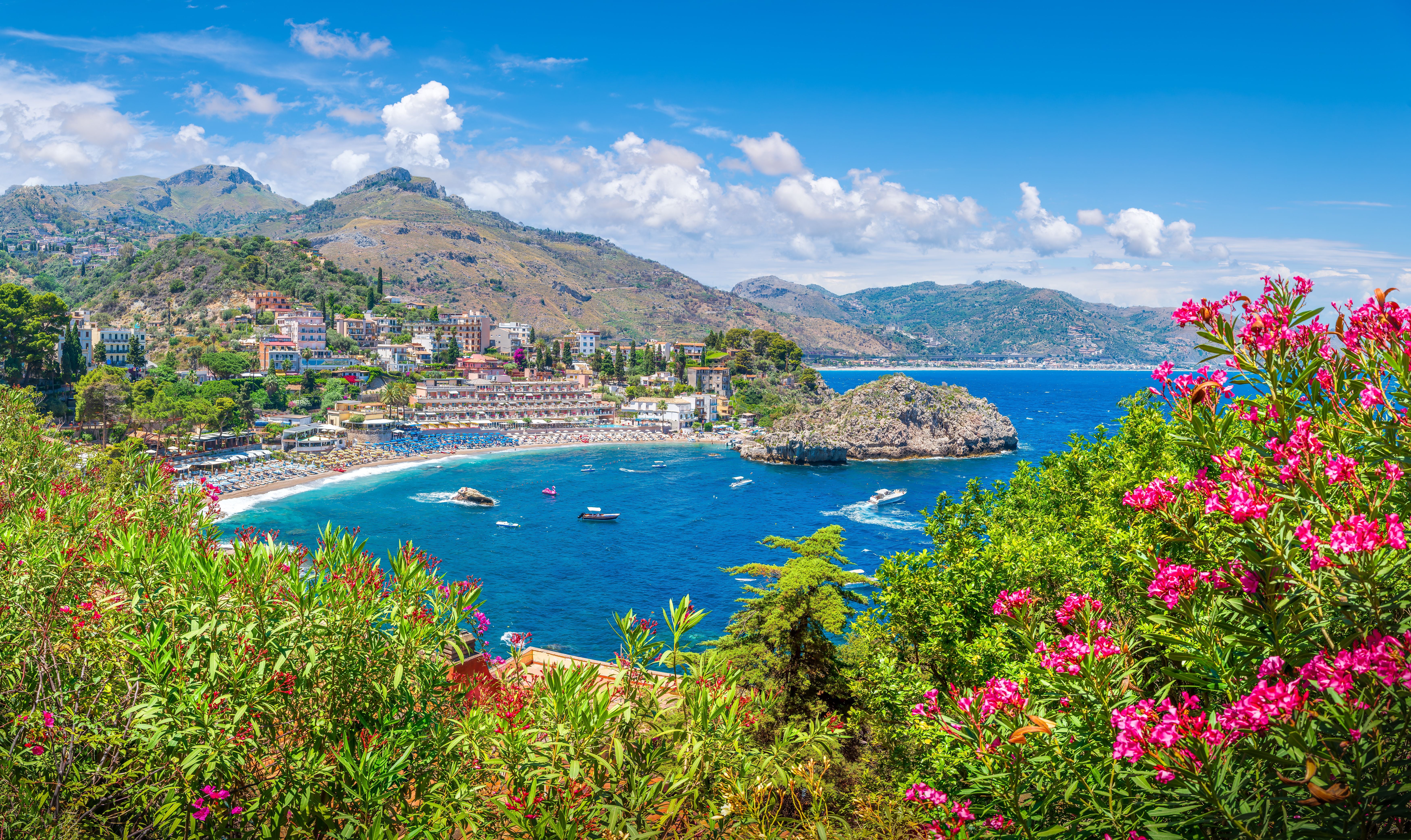Blick auf Mazzarò-Strand bei Taormina mit blauem Meer, Bergen und blühenden Sträuchern.