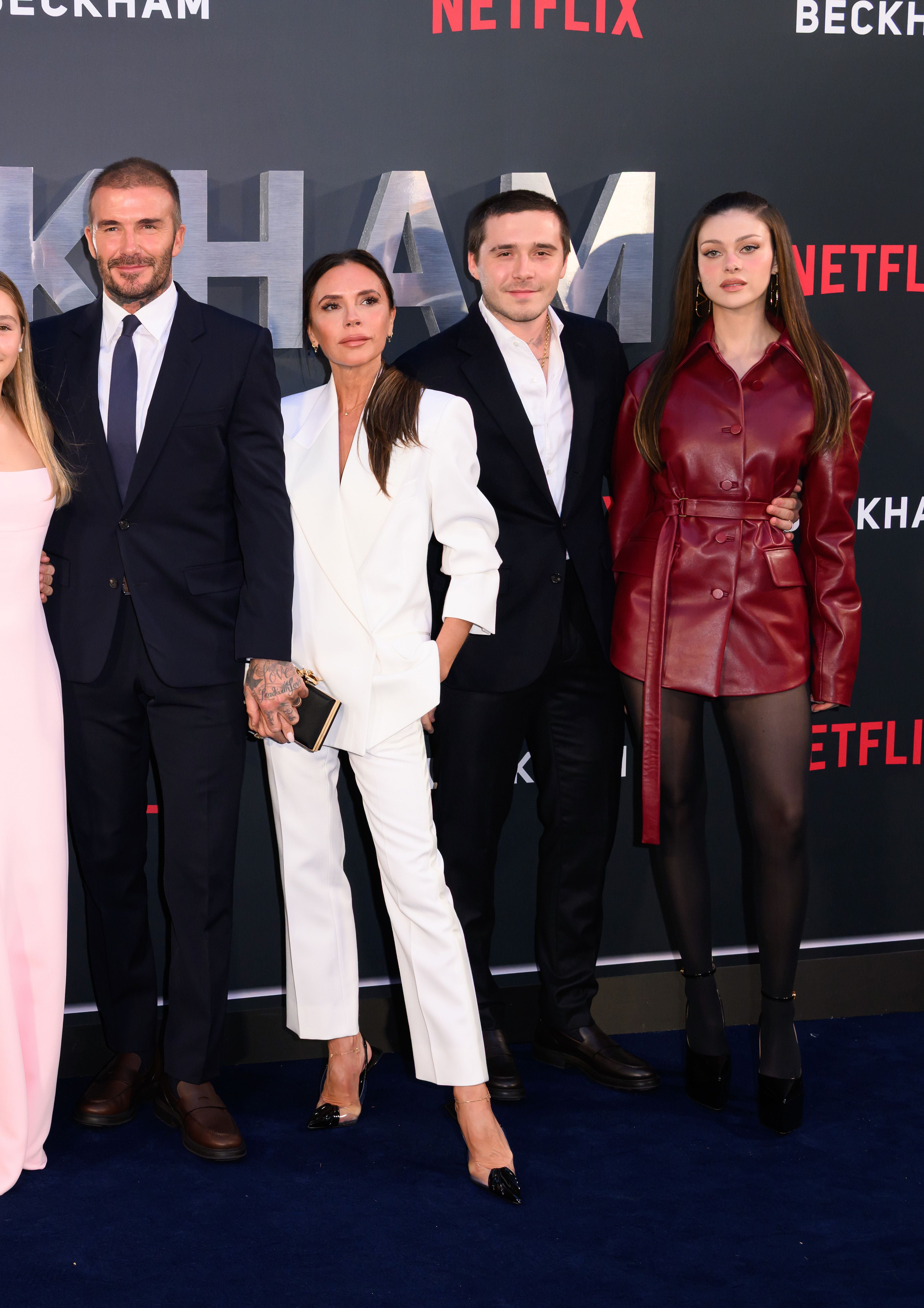Vier elegant gekleidete Personen posieren gemeinsam auf dem roten Teppich vor Netflix-Logos.