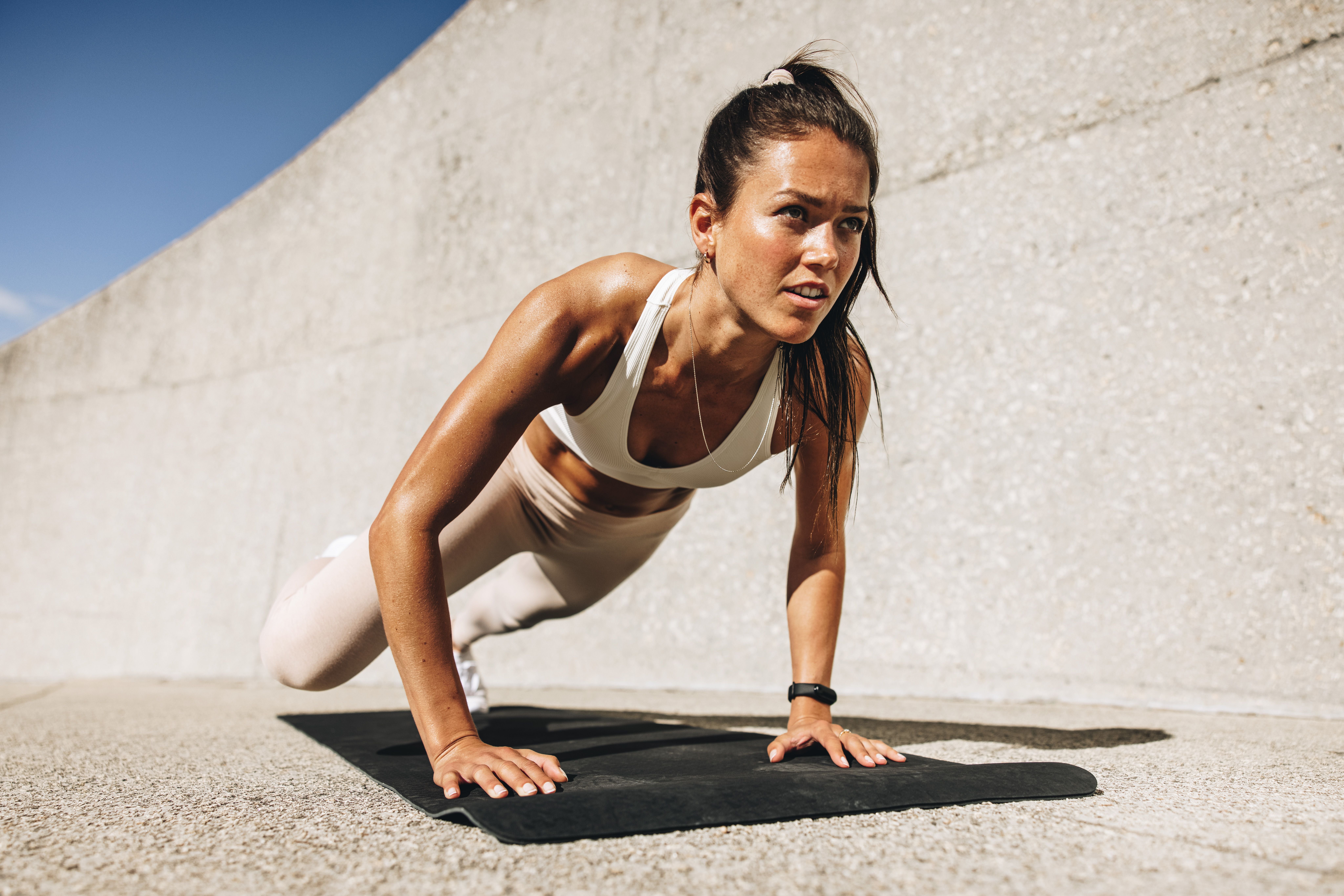 Sportliche Frau macht draußen Mountain Climbers auf einer Fitnessmatte vor einer Betonwand.