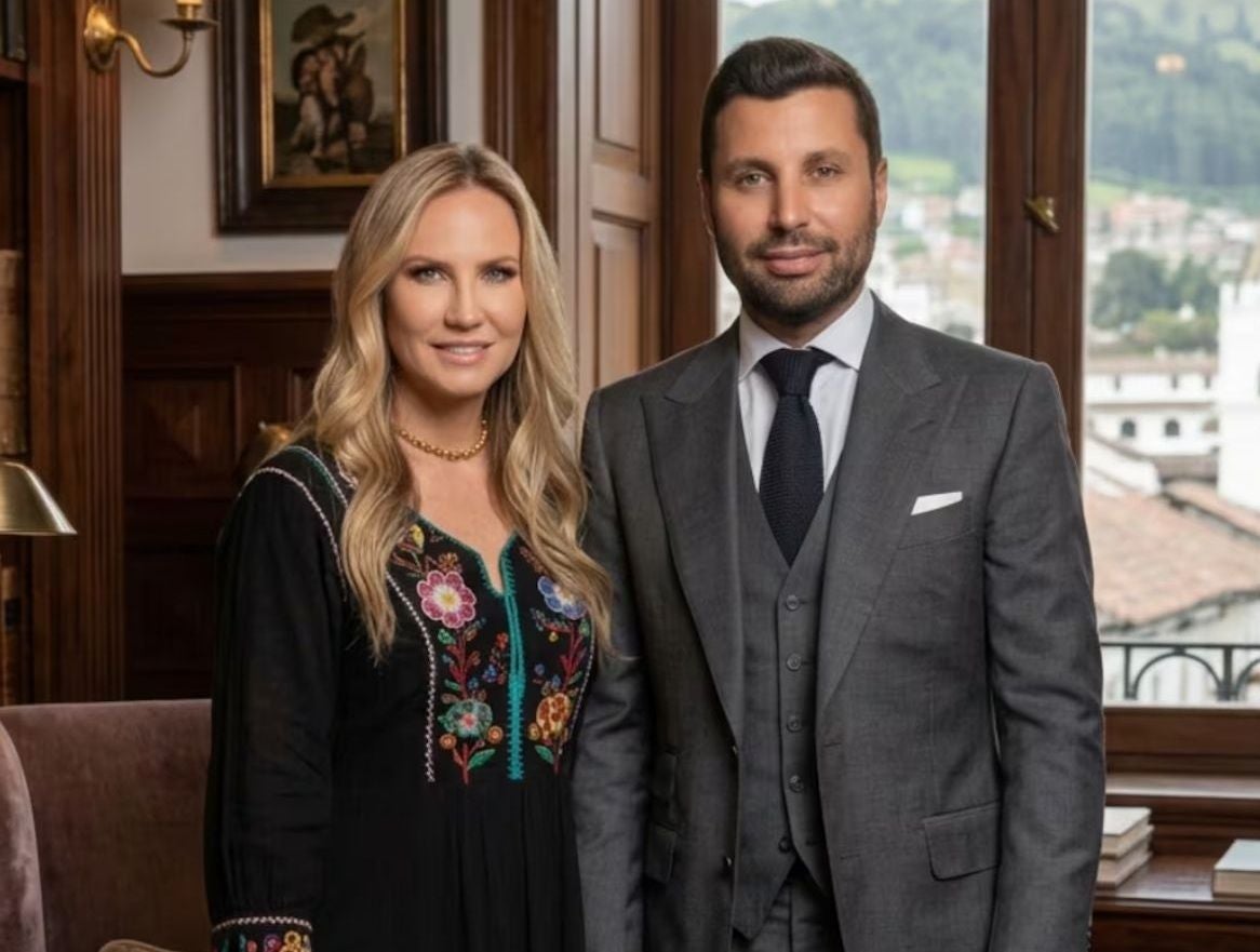 Ein Mann im grauen Anzug und eine Frau im schwarzen Kleid mit Blumenmuster posieren in einem eleganten Raum.