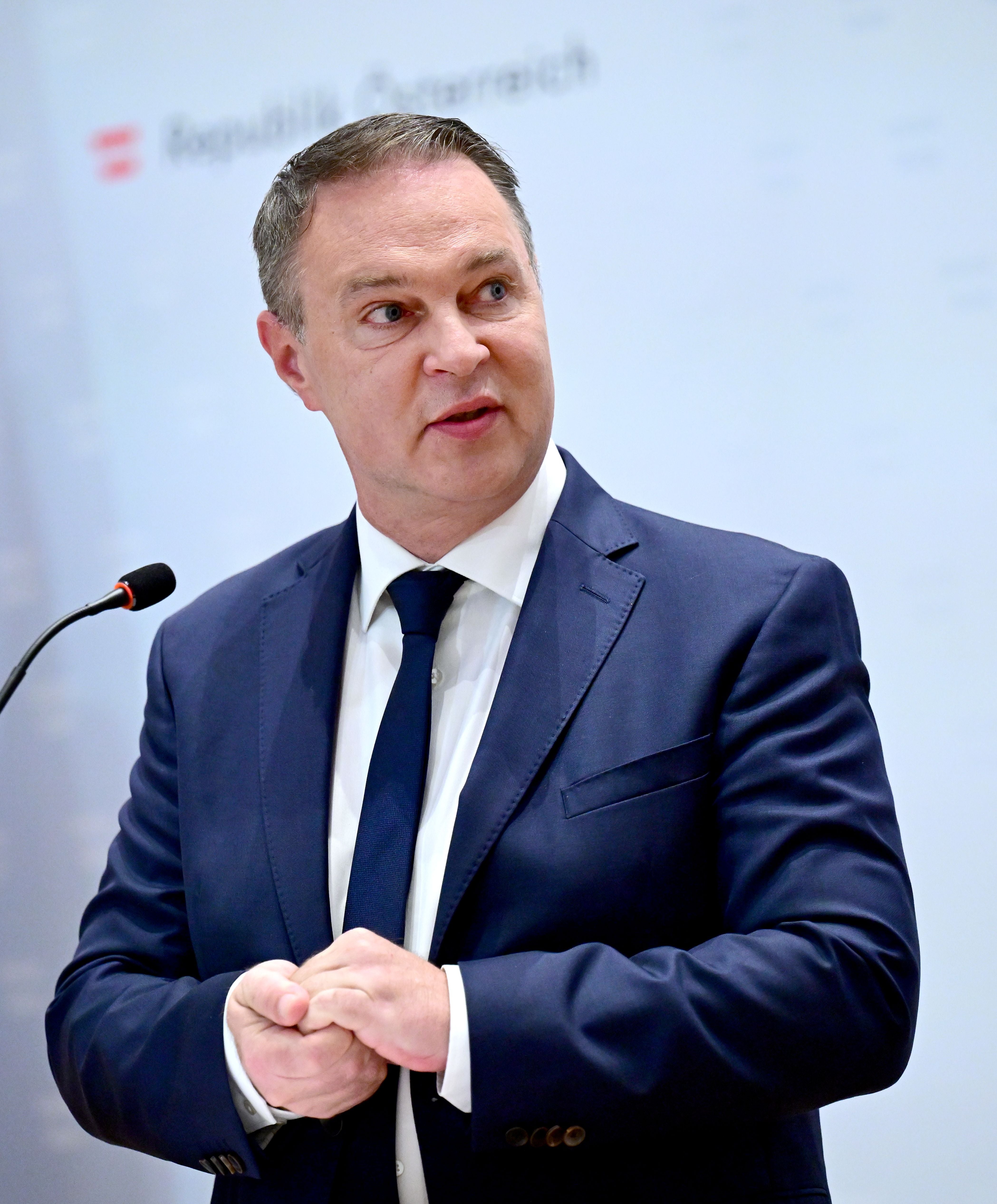 Ein Mann im Anzug spricht bei einer Pressekonferenz an einem Mikrofon.