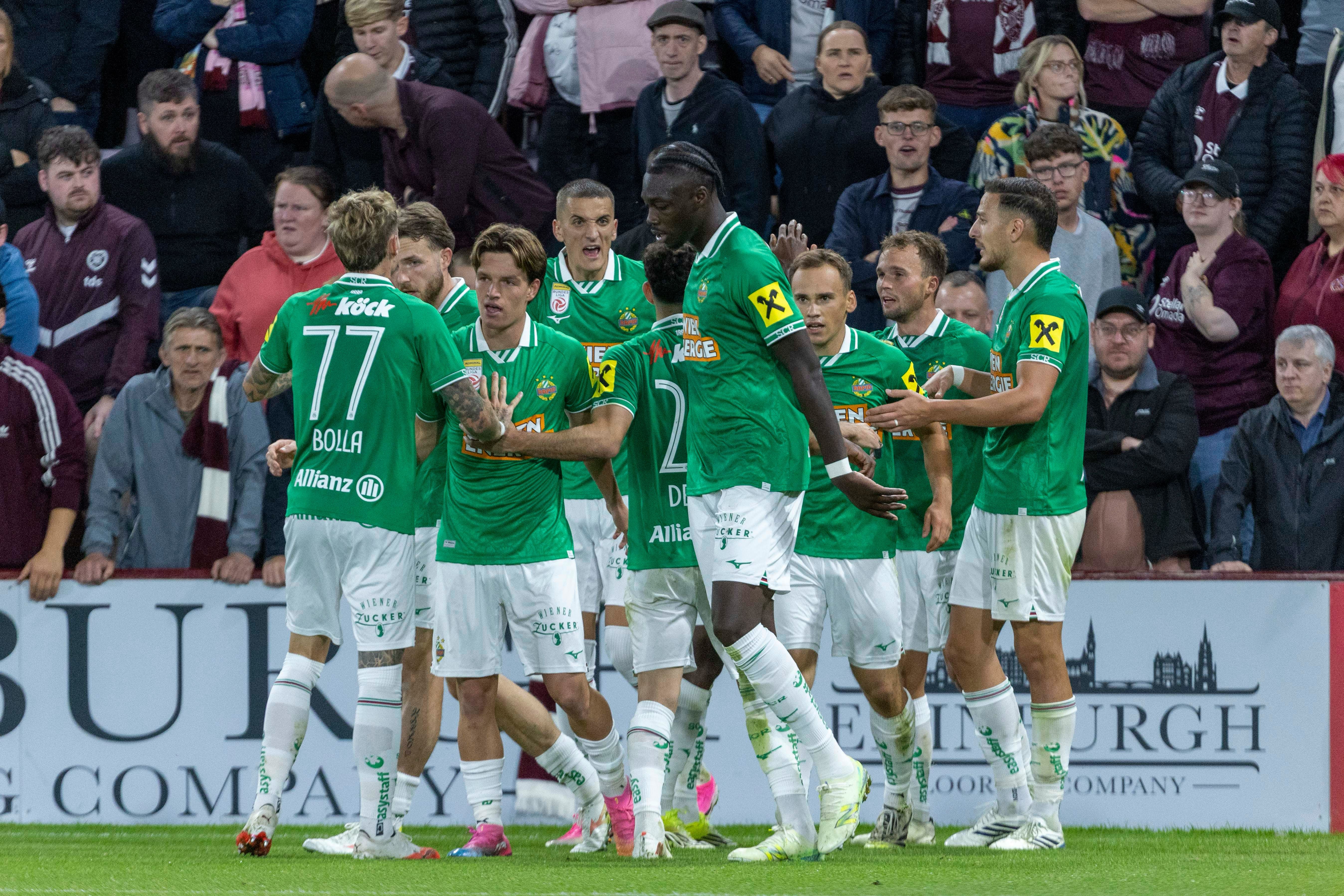 Nikolaus Wurmbrand und seine Teamkollegen vom SK Rapid im grünen Trikot jubeln gemeinsam auf dem Rasen im Stadion von Edinburgh.